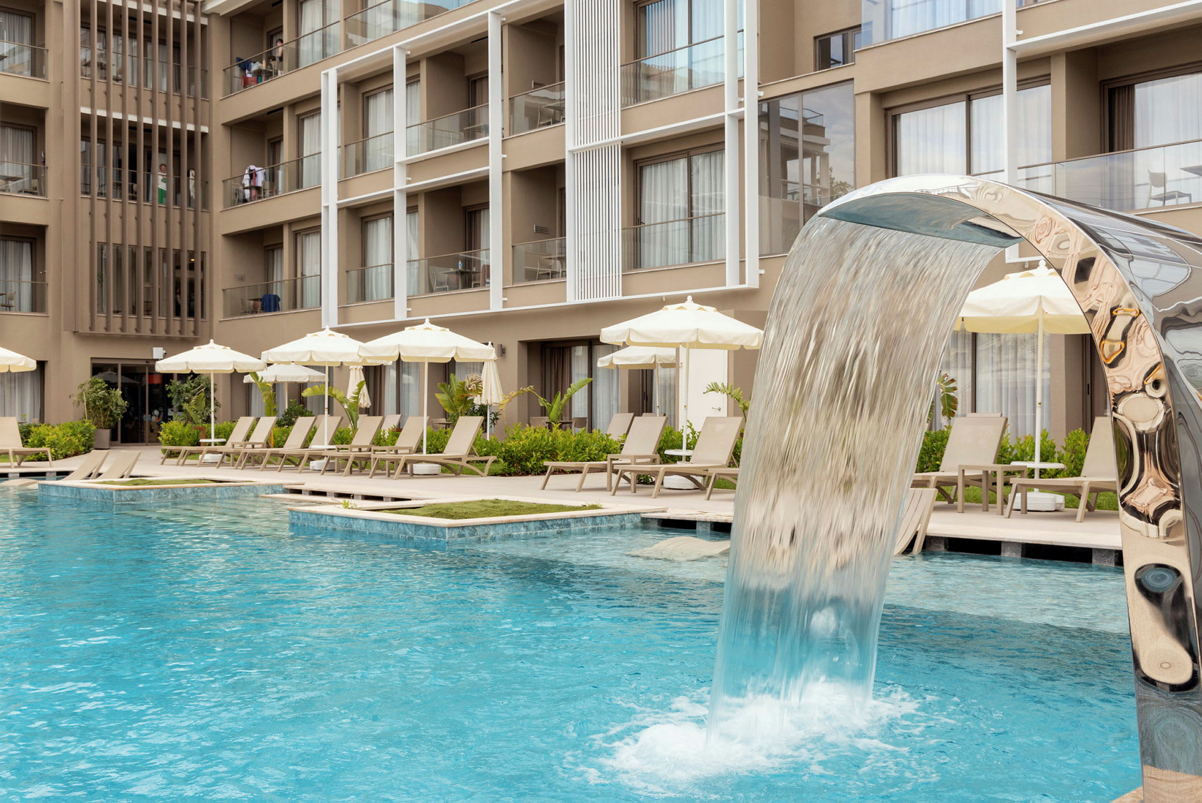 Hotellpool med vattenfall samt solstolar och parasoller vid kanten. (AI-genererad text)