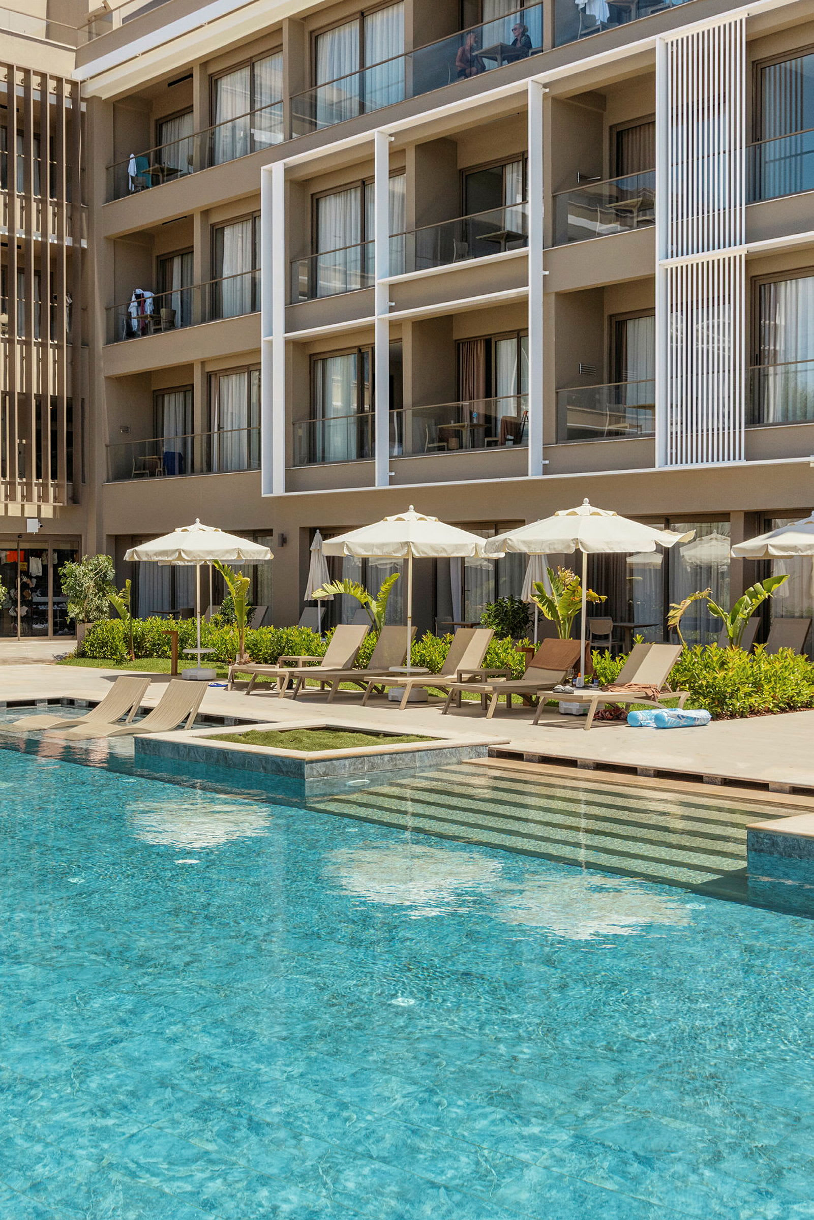 En hotellfasad med balkonger och en pool med solstolar och parasoller. (AI-genererad text)