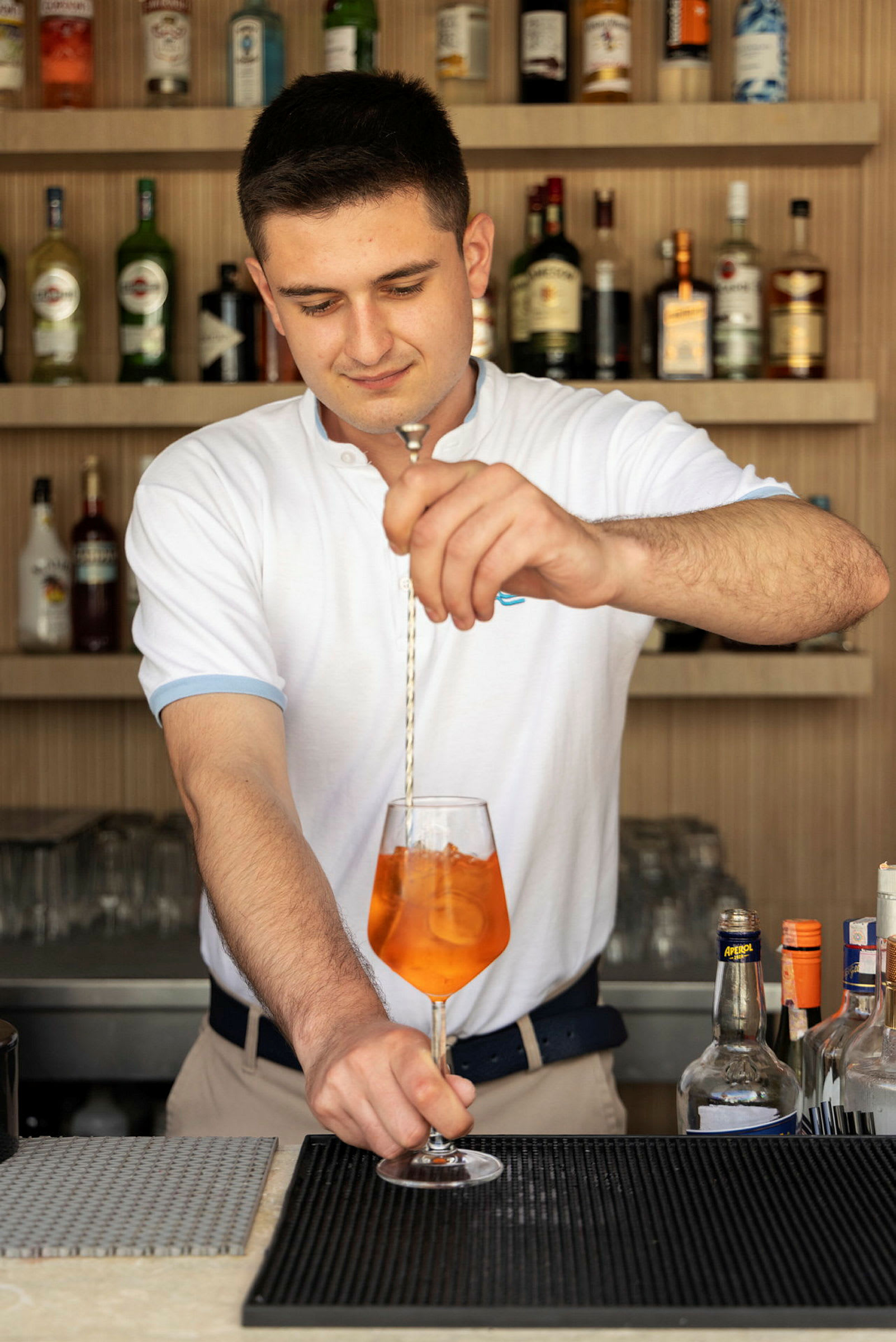 En bartender blandar en drink med orange vätska i ett vinglas. (AI-genererad text)