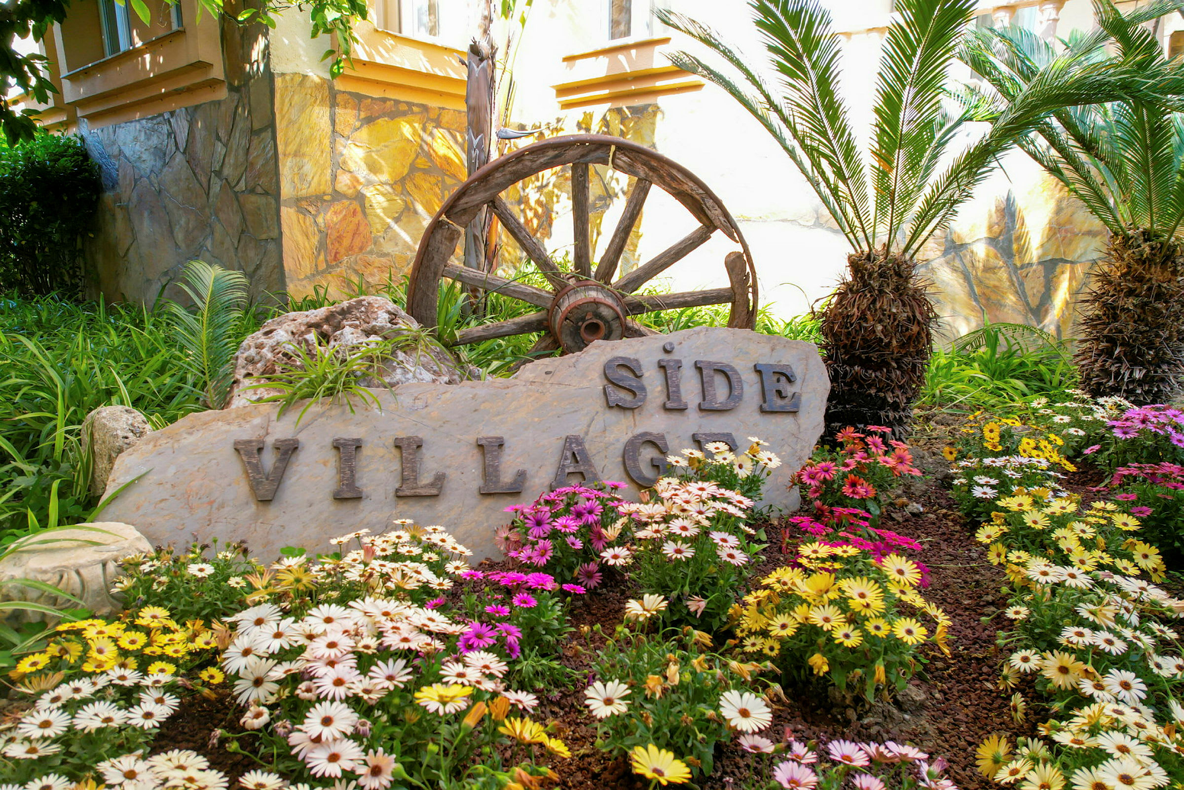 En sten med texten 'Side Village' omgiven av blommor och palmer. (AI-genererad text)