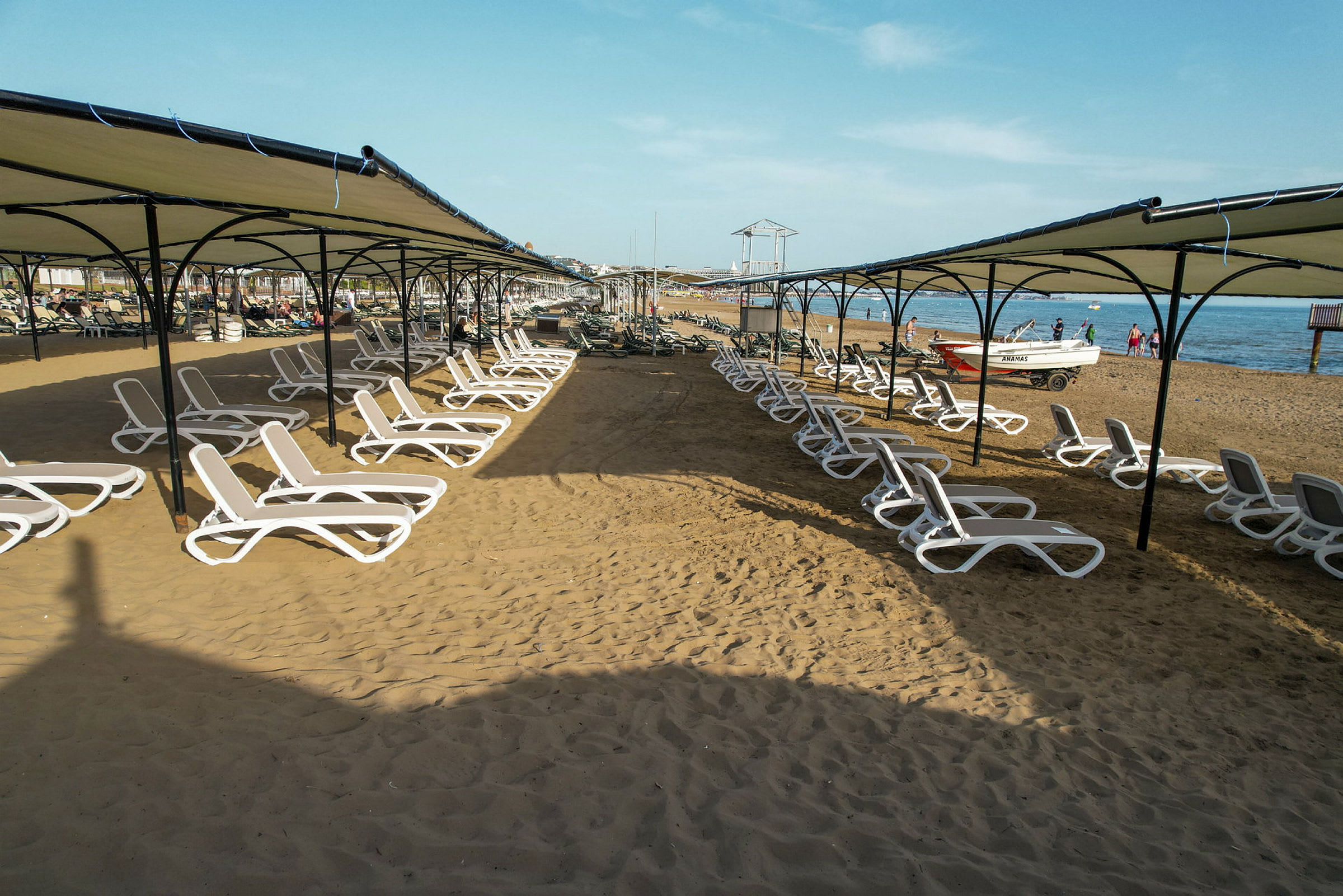 Solstolar under skuggande tak på en sandstrand vid havet. (AI-genererad text)