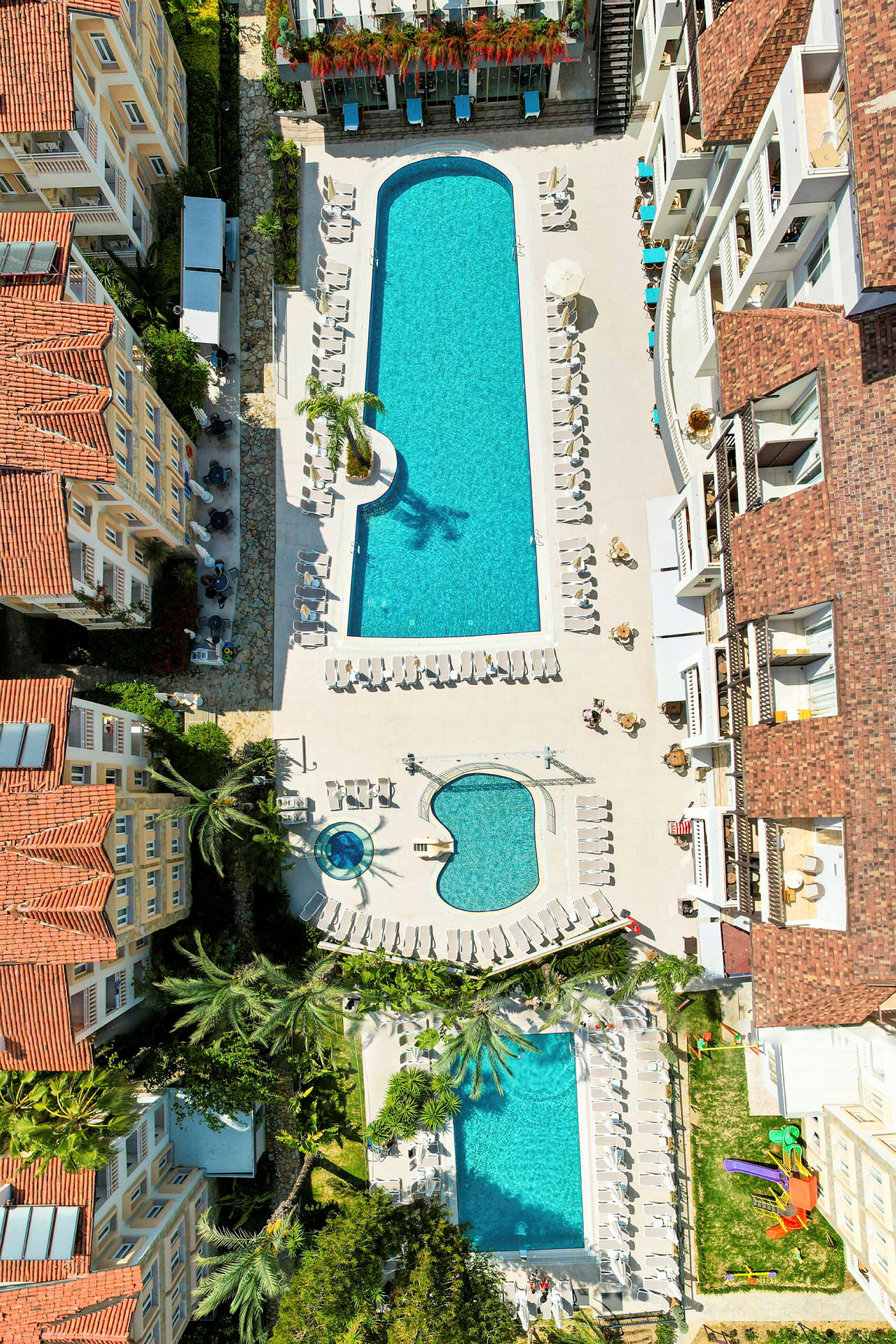 Fågelperspektiv av hotellområde med flera pooler och solstolar. (AI-genererad text)