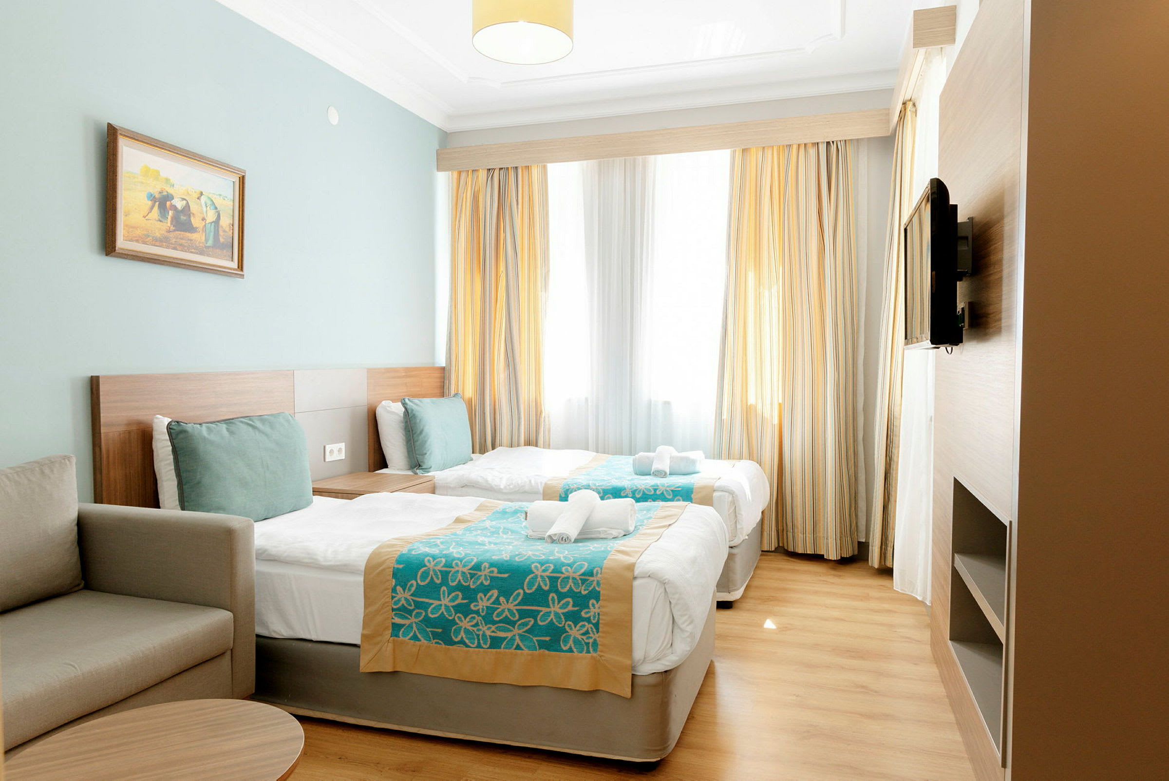 Hotellrum med två enkelsängar, en soffa och en TV på väggen. (AI-genererad text)