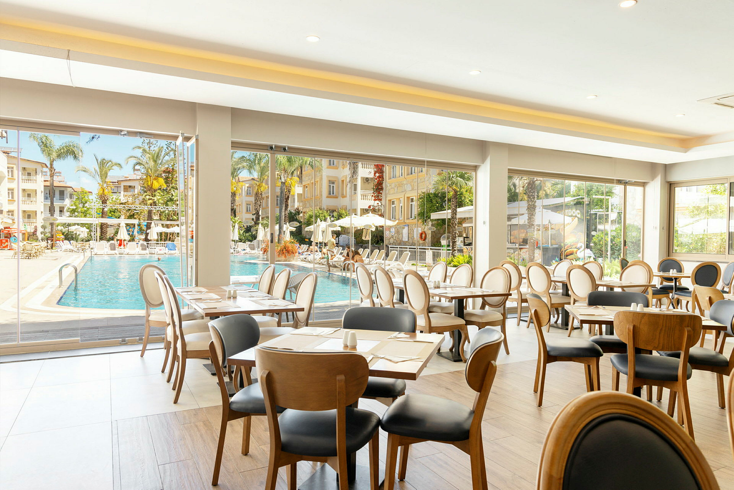 Interiör av restaurang med utsikt mot poolområde och palmer. (AI-genererad text)