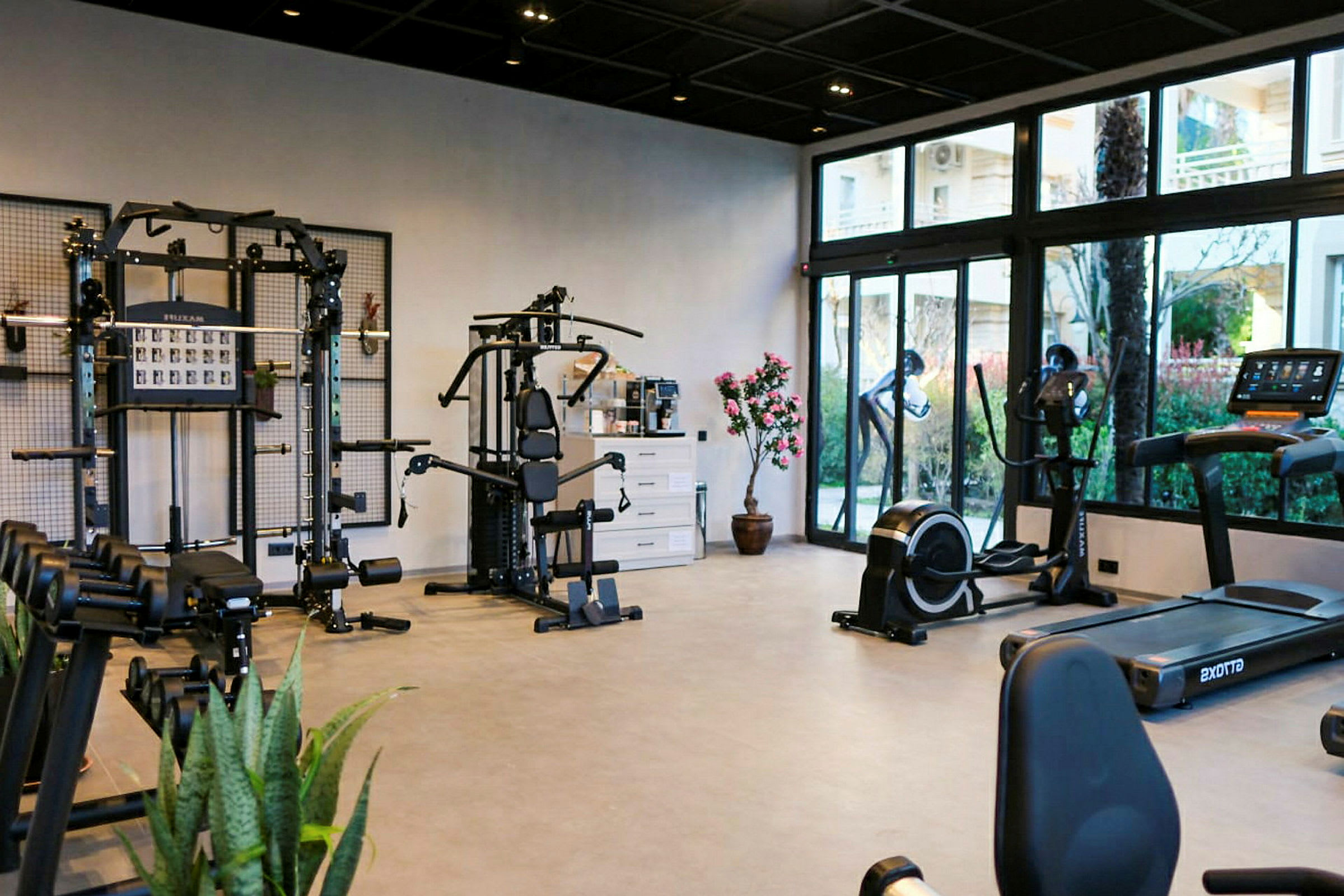 Ett gym med olika träningsmaskiner och vikter, samt glasfönster som visar utsikten utanför. (AI-genererad text)