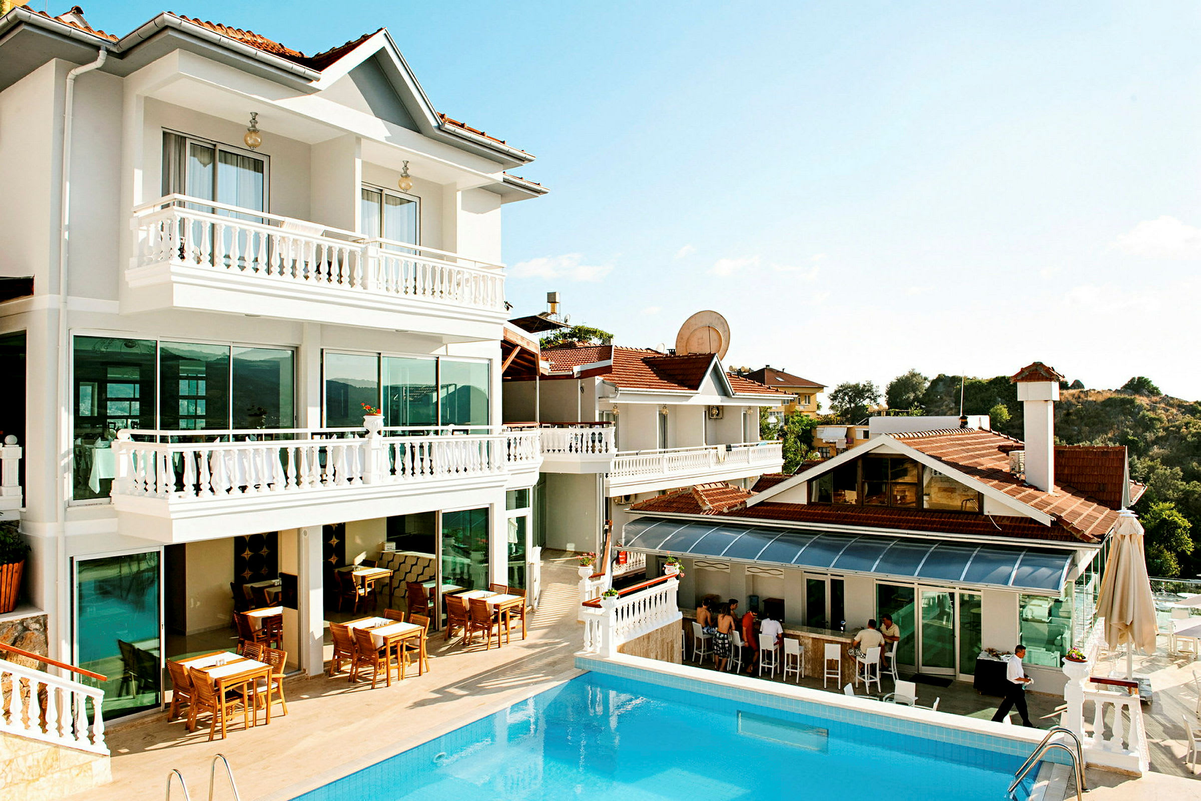 Hotellbyggnad med vit fasad, bord utomhus och pool. (AI-genererad text)