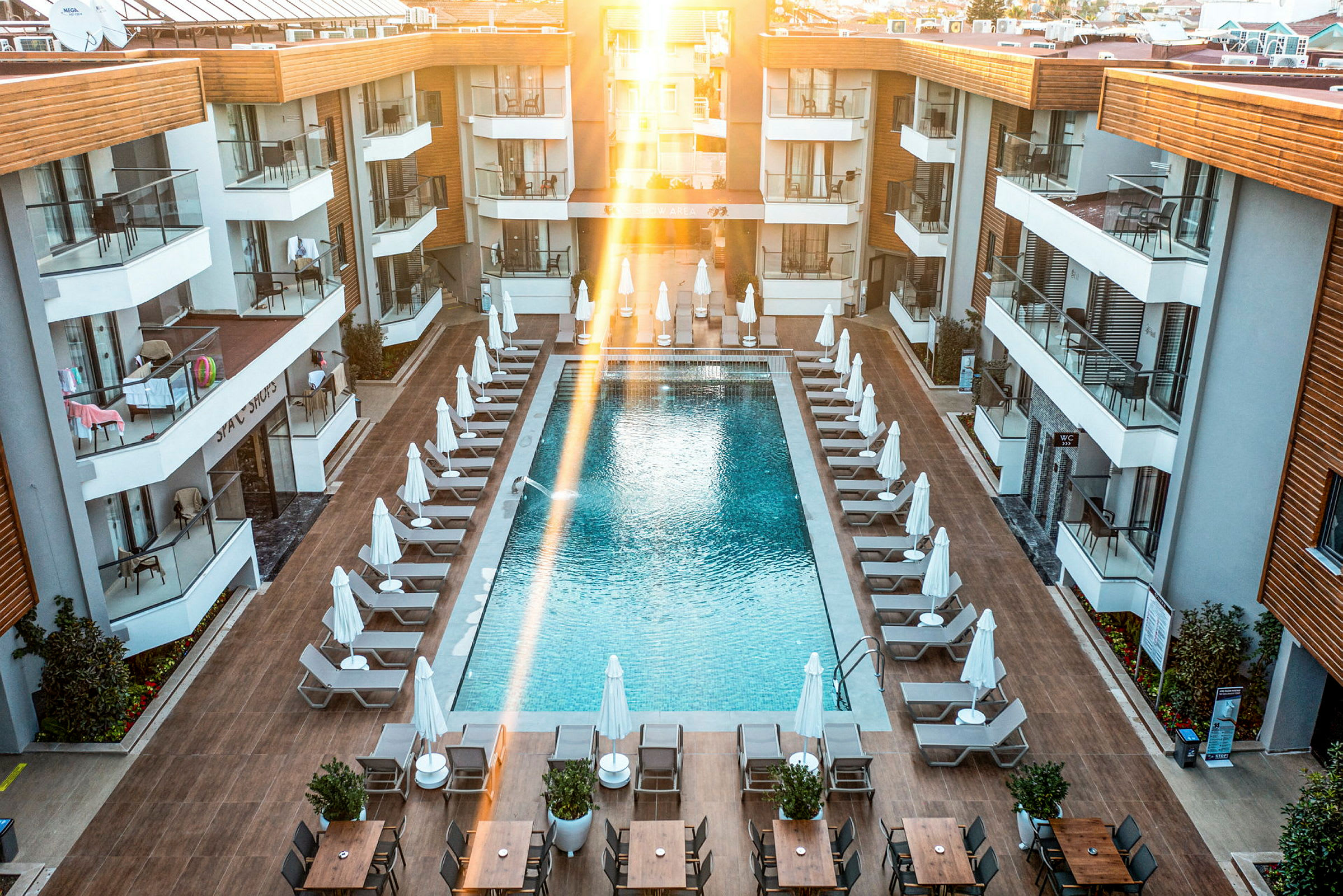 Bild av ett hotellpoolområde med solstolar och parasoller runt en rektangulär pool, omgiven av moderna hotellbyggnader. (AI-genererad text)