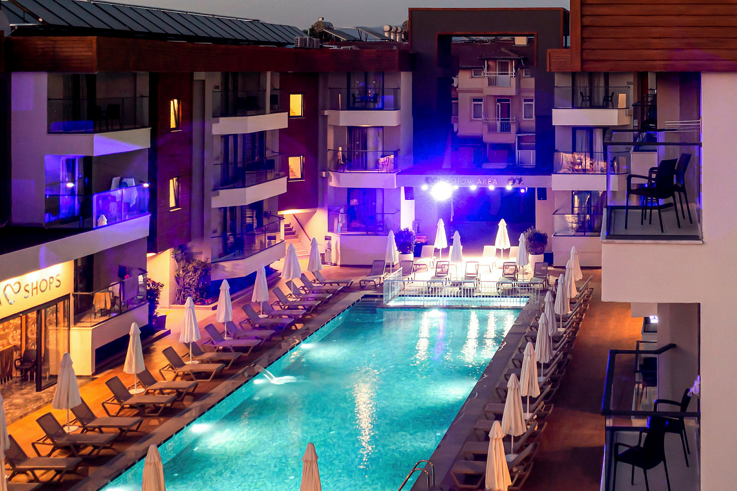 Utsikt över en upplyst pool på kvällen, omgiven av solstolar och parasoller vid ett hotell. (AI-genererad text)