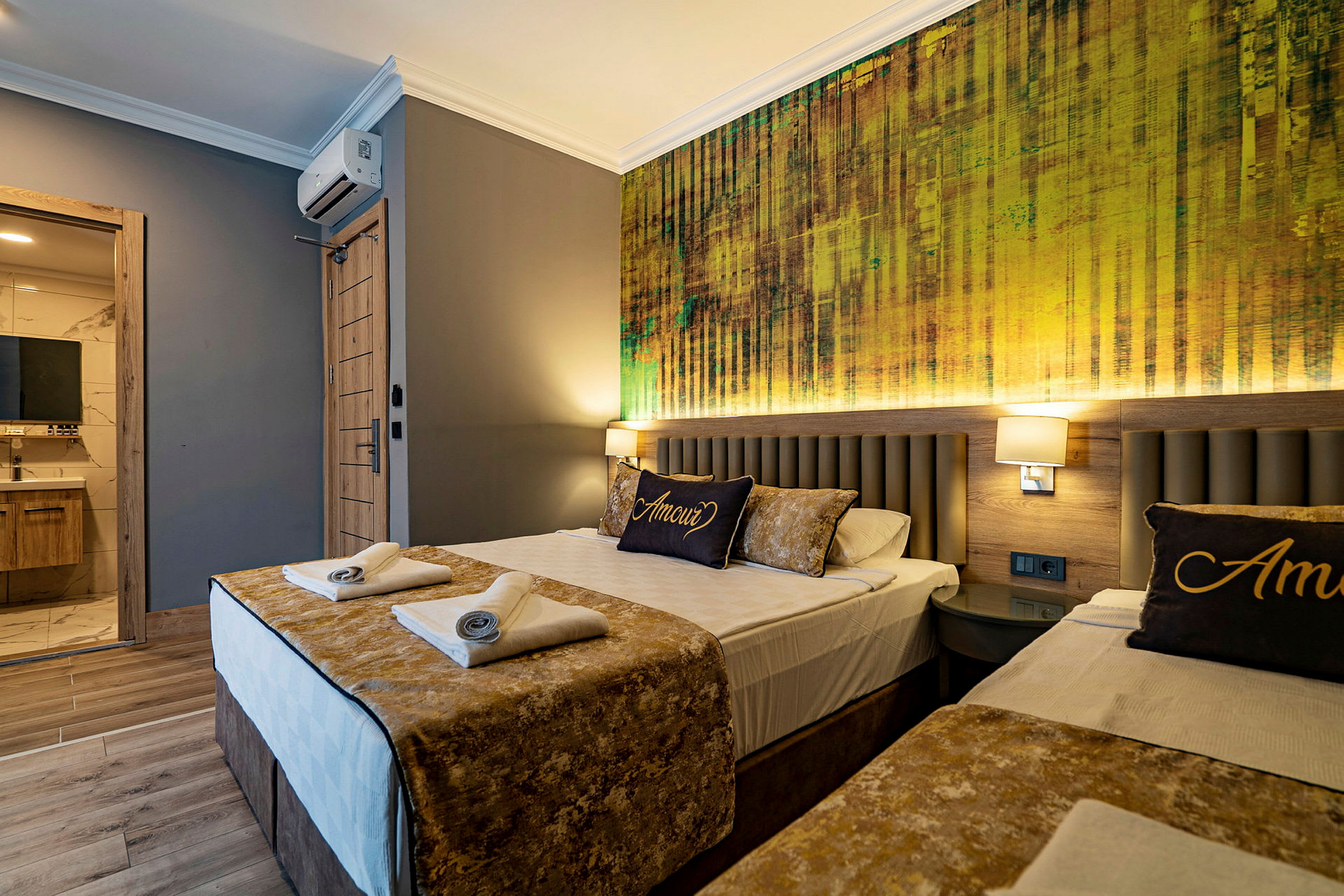 Ett hotellrum med två bäddar, luftigt dekorerat med gyllene accenter och en vägg med modern textur bakom sängarna. (AI-genererad text)