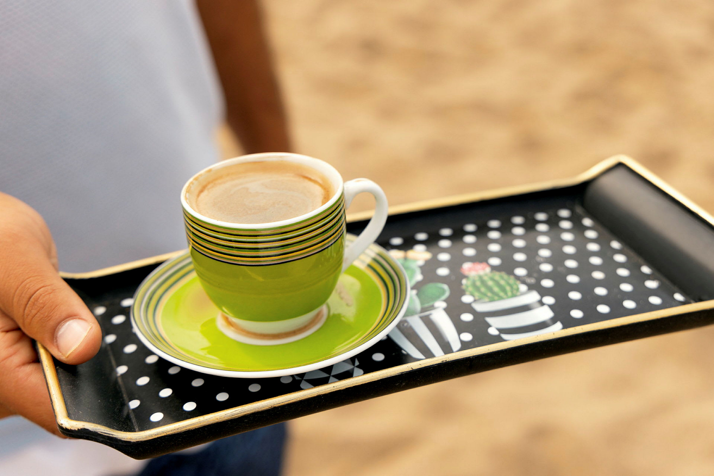 En hand håller en bricka med en färgglad kopp kaffe och fat. (AI-genererad text)