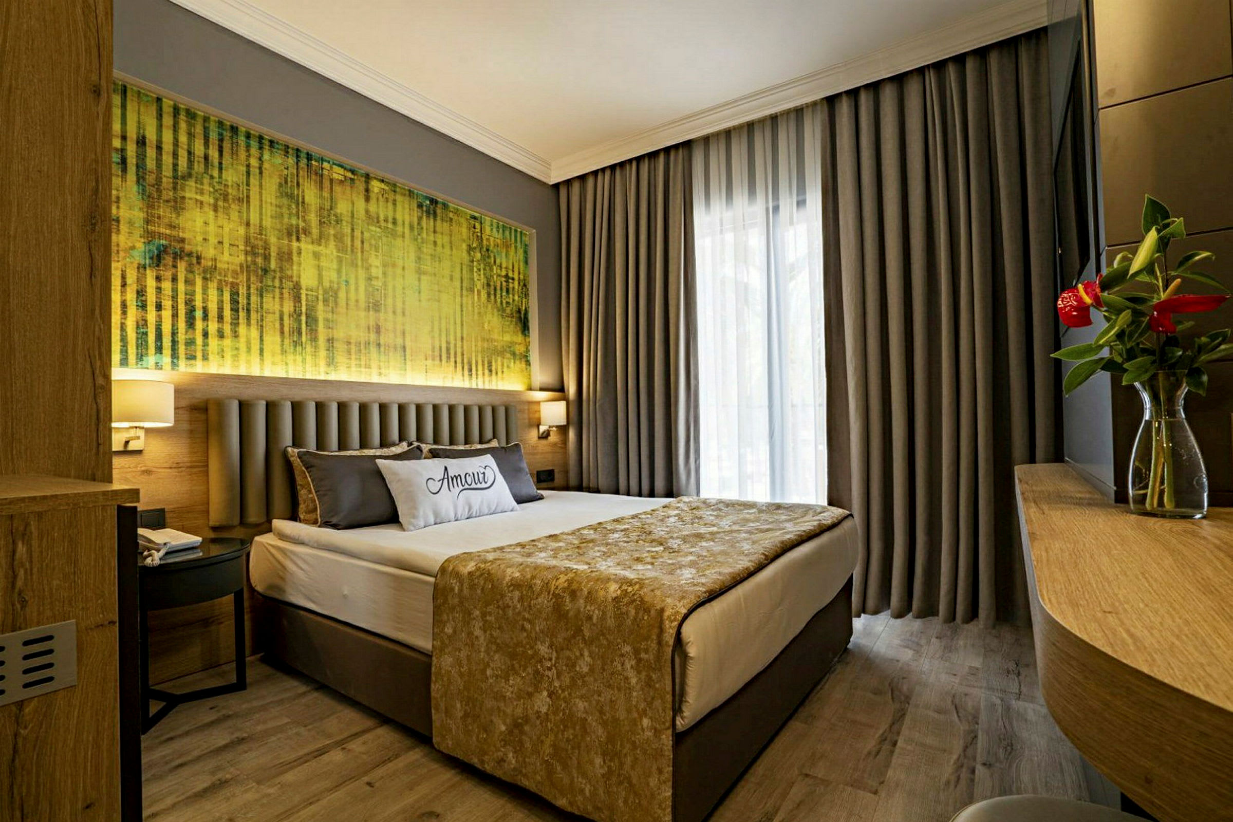Ett hotellrum med en dubbelsäng, grå gardiner och en tavla ovanför sängen. (AI-genererad text)