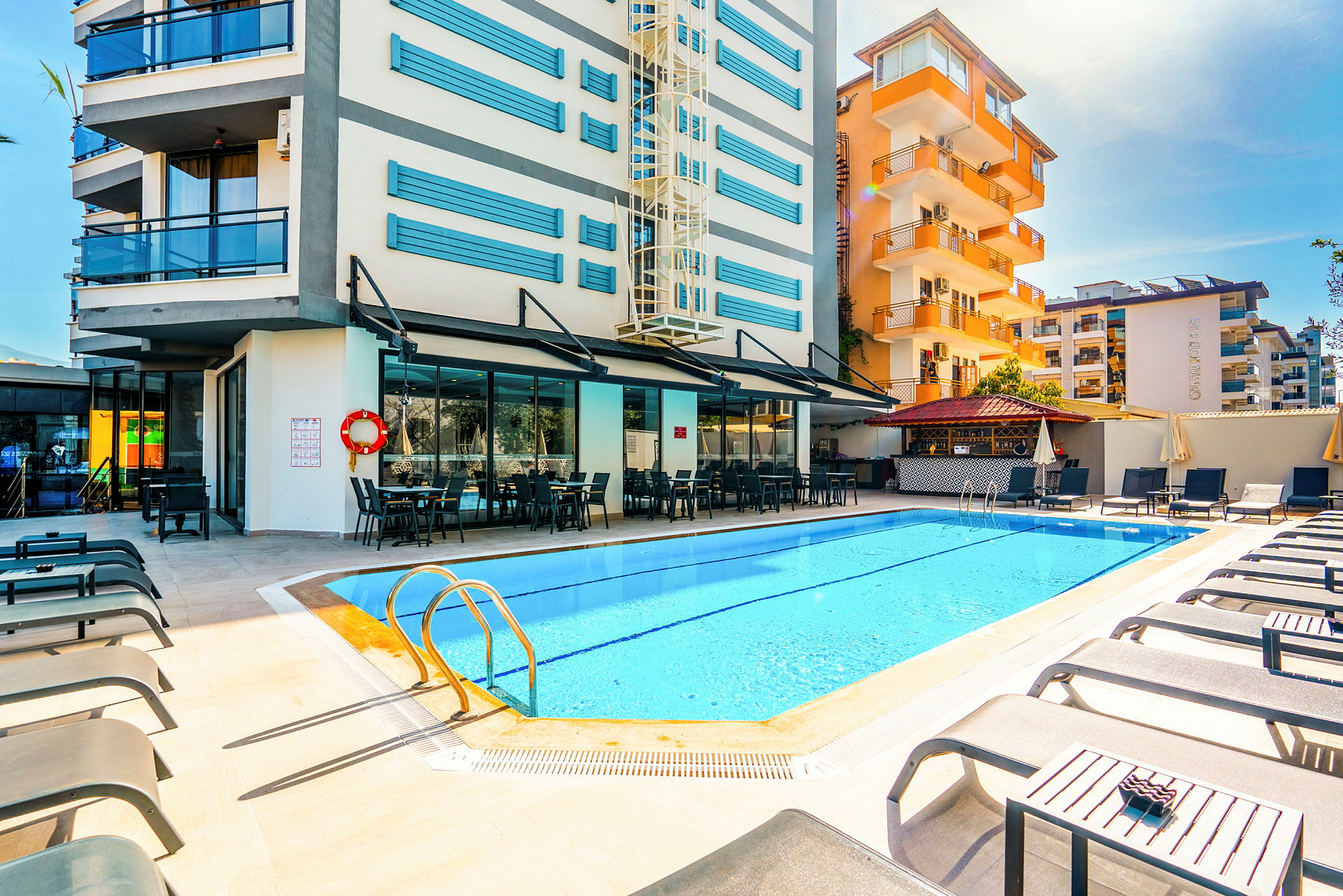 Poolområde vid hotell med solstolar och uteservering. (AI-genererad text)