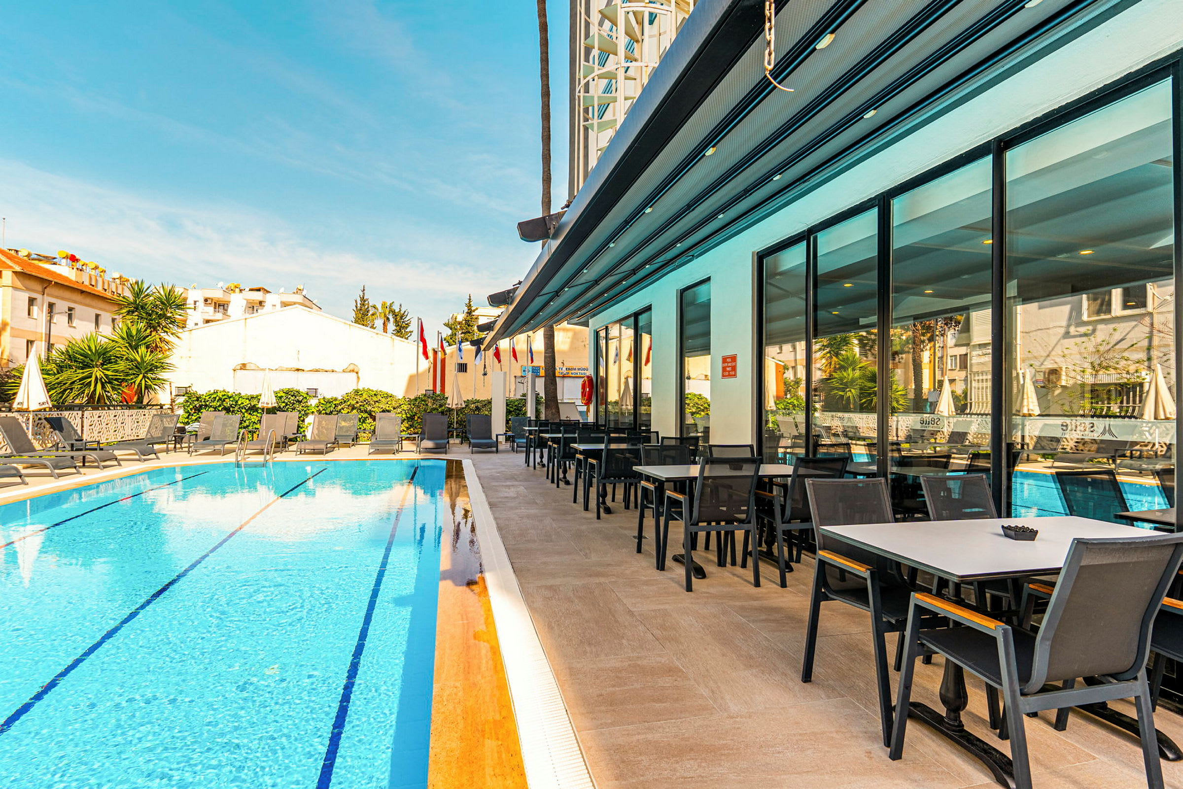 En hotellpool med solstolar och ett angränsande matområde. (AI-genererad text)