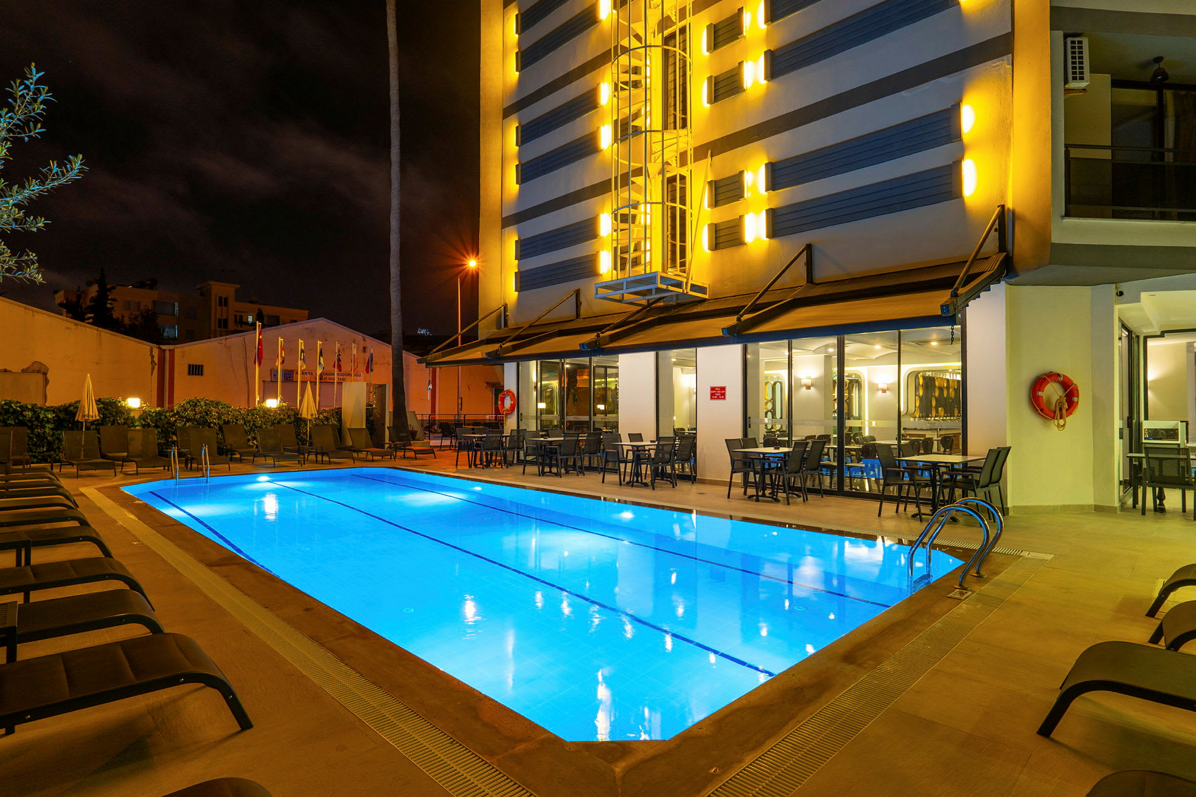 Utomhuspool vid ett hotell på kvällen, omgiven av solstolar och bord. (AI-genererad text)
