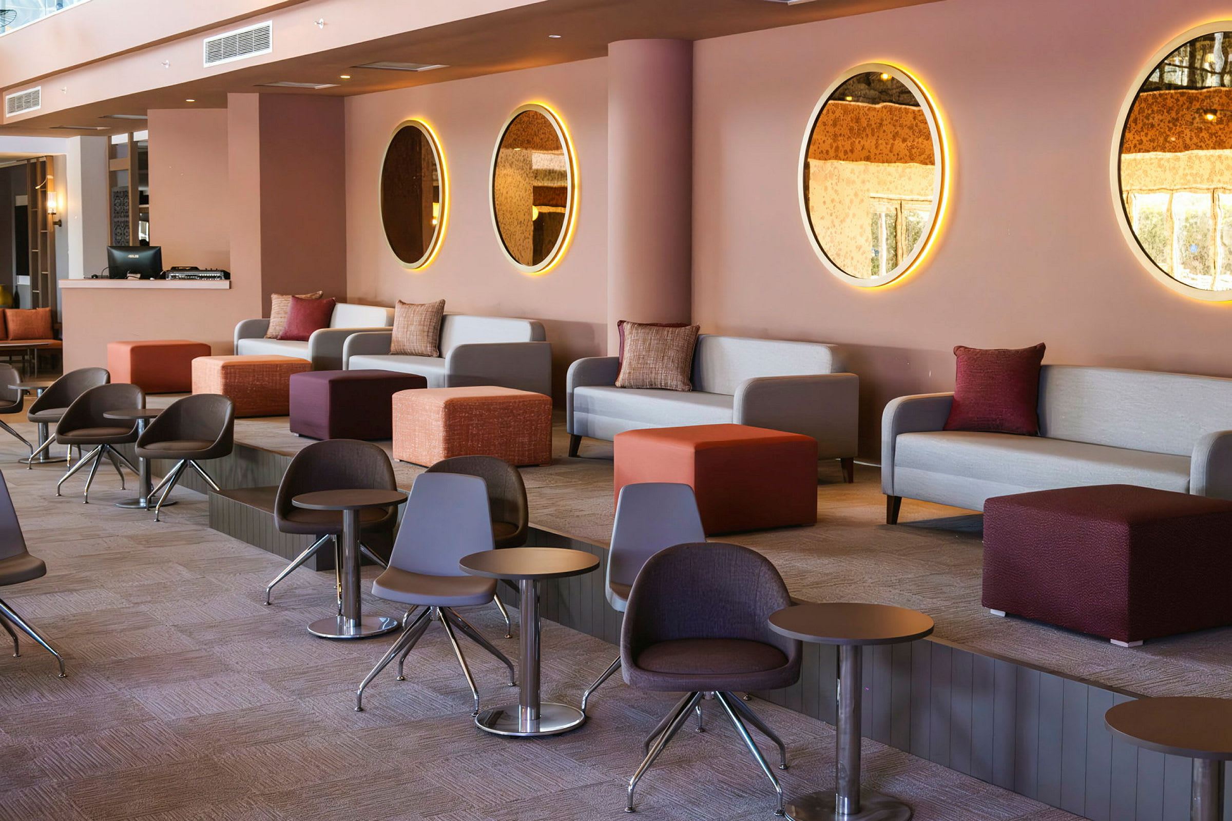 En modern och färgglad lounge med soffor, små bord och runda speglar på väggen. (AI-genererad text)