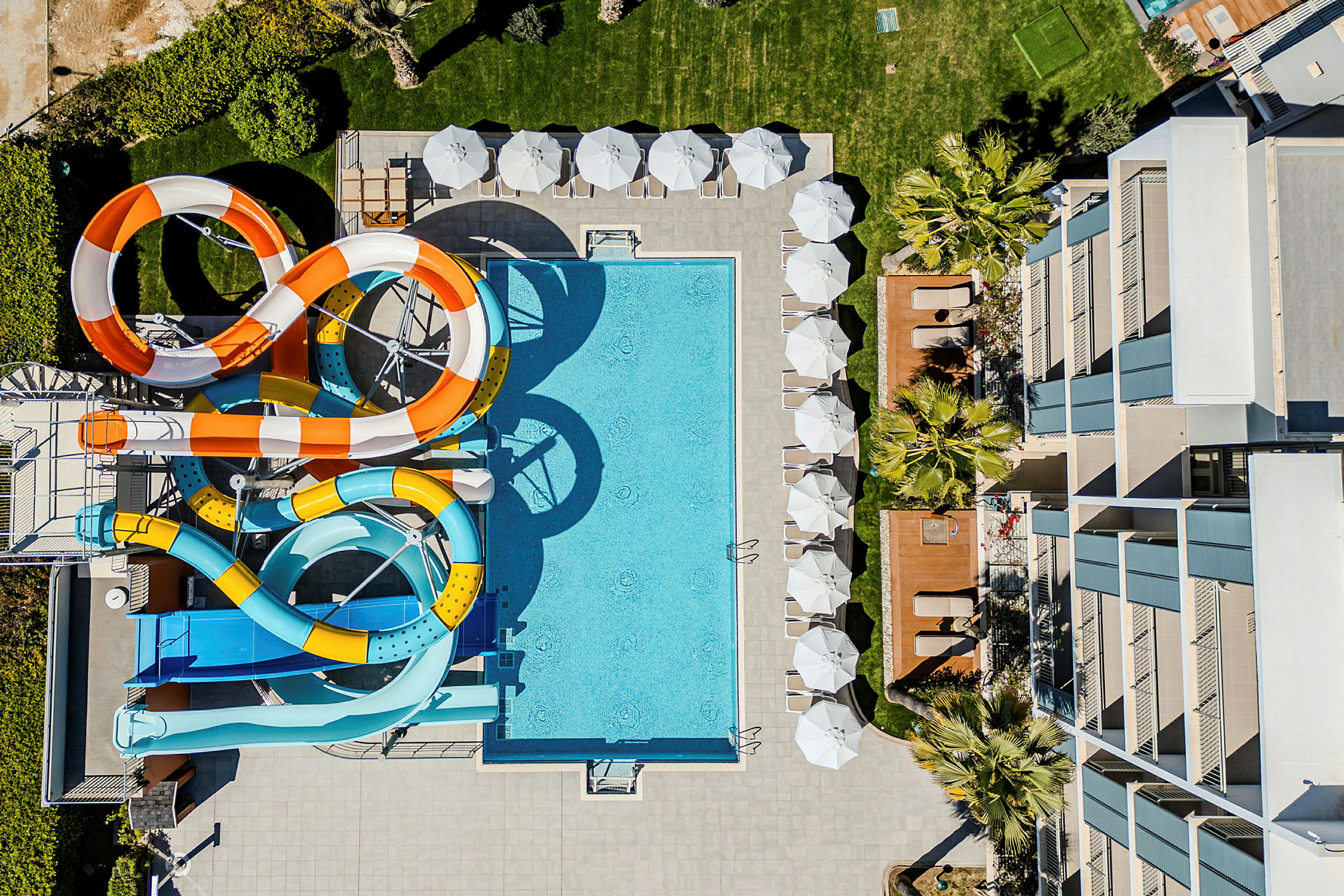 Vy uppifrån av en hotellpool med färgglada vattenrutschkanor och solstolar. (AI-genererad text)