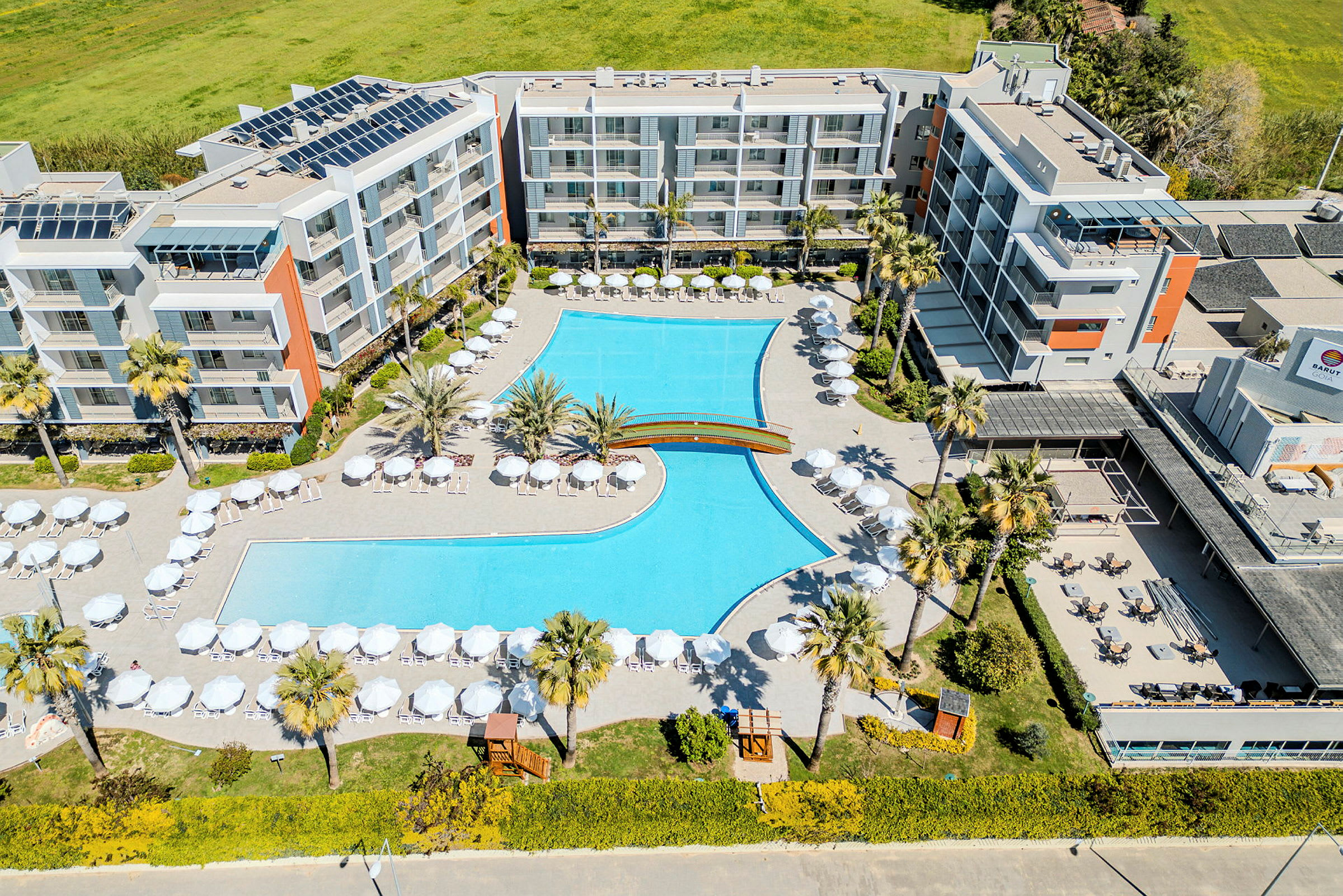 Flygbild av ett hotellområde med en stor pool omgiven av parasoller och solstolar. (AI-genererad text)