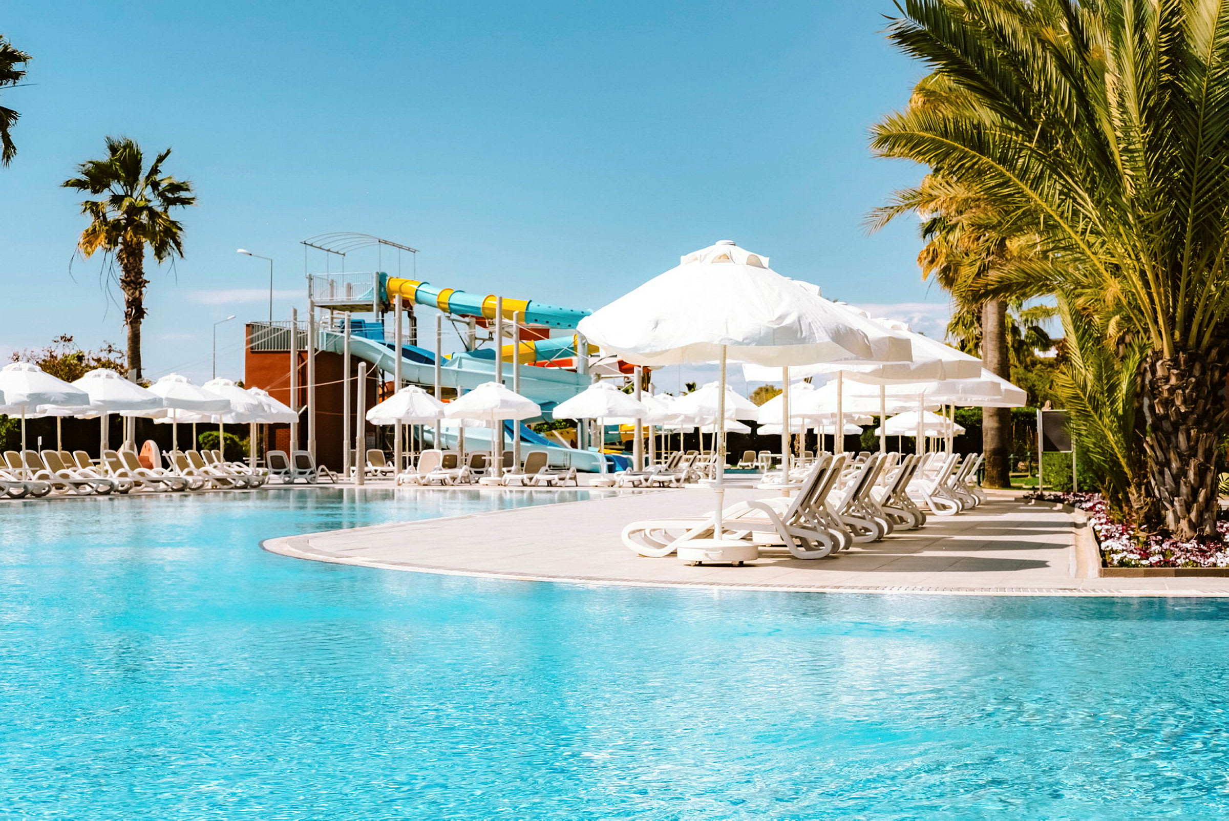 En swimmingpool med solstolar, parasoller och vattenrutschbanor. (AI-genererad text)
