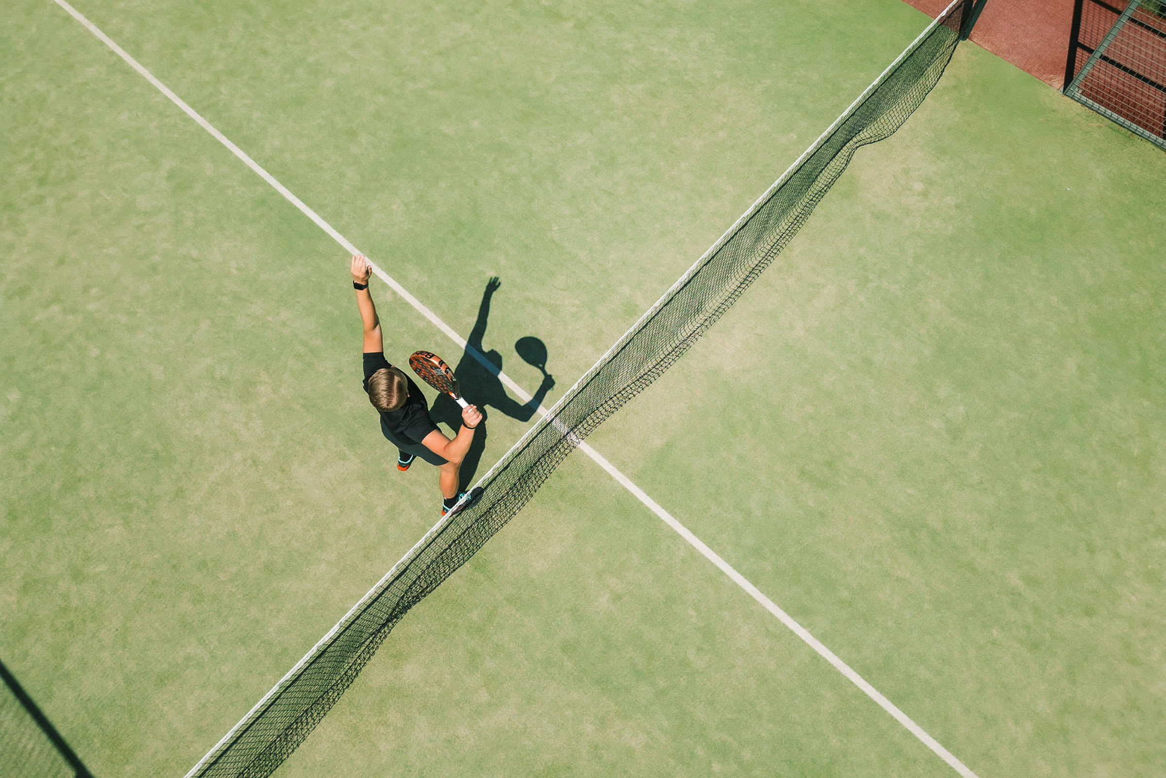 En person spelar tennis på en grön bana och är i färd med att slå en boll med en racket. (AI-genererad text)