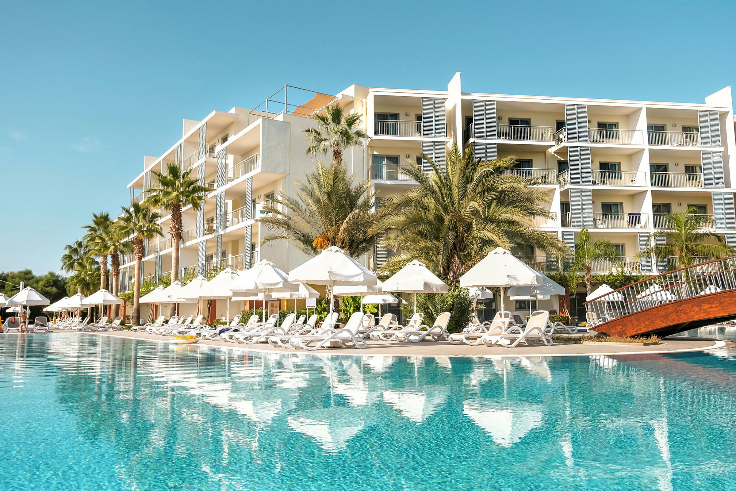 En hotellbyggnad bredvid en stor pool med solstolar och parasoller. (AI-genererad text)