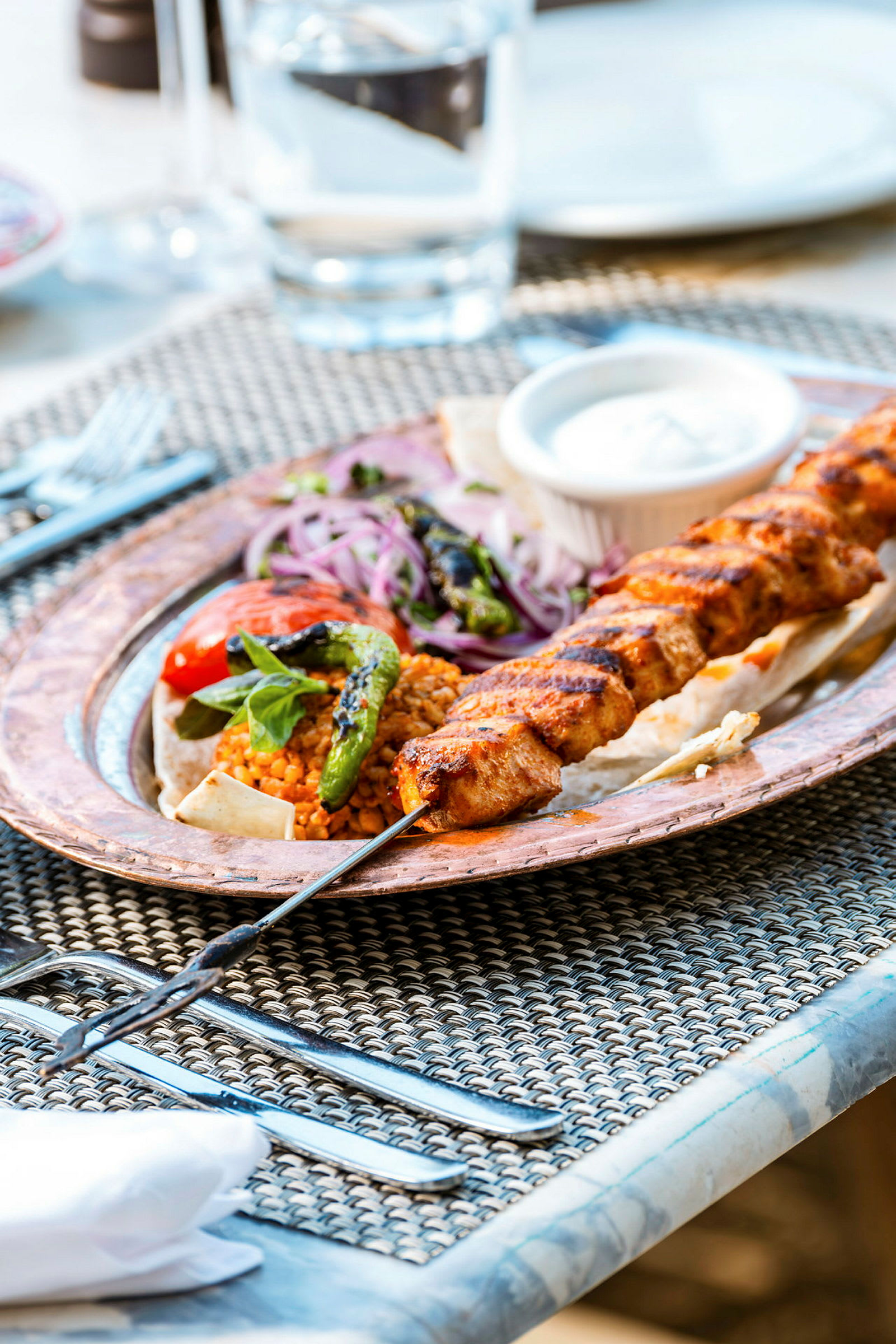 En tallrik med grillspett, grönsaker och sås på ett bord. (AI-genererad text)