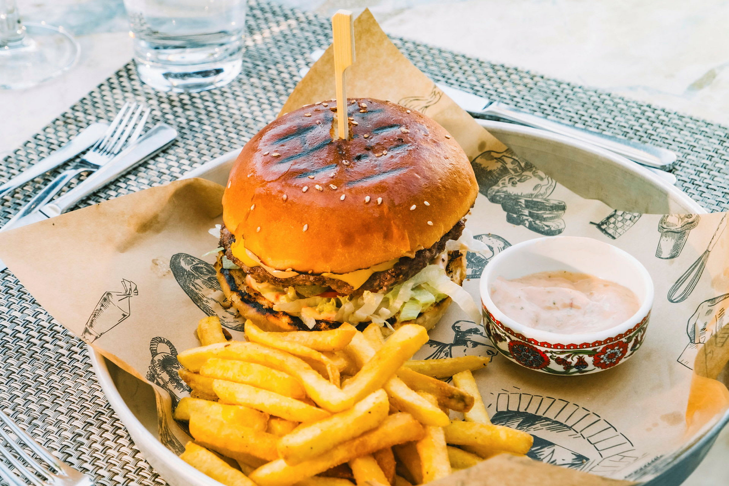 En hamburgare serverad på en tallrik med pommes frites och en skål sås. (AI-genererad text)
