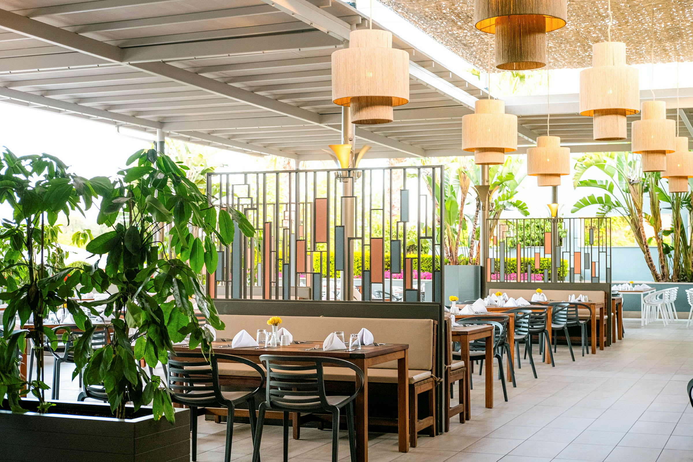 Bild av en utomhusrestaurang med flera bord, stolar och grönska. (AI-genererad text)