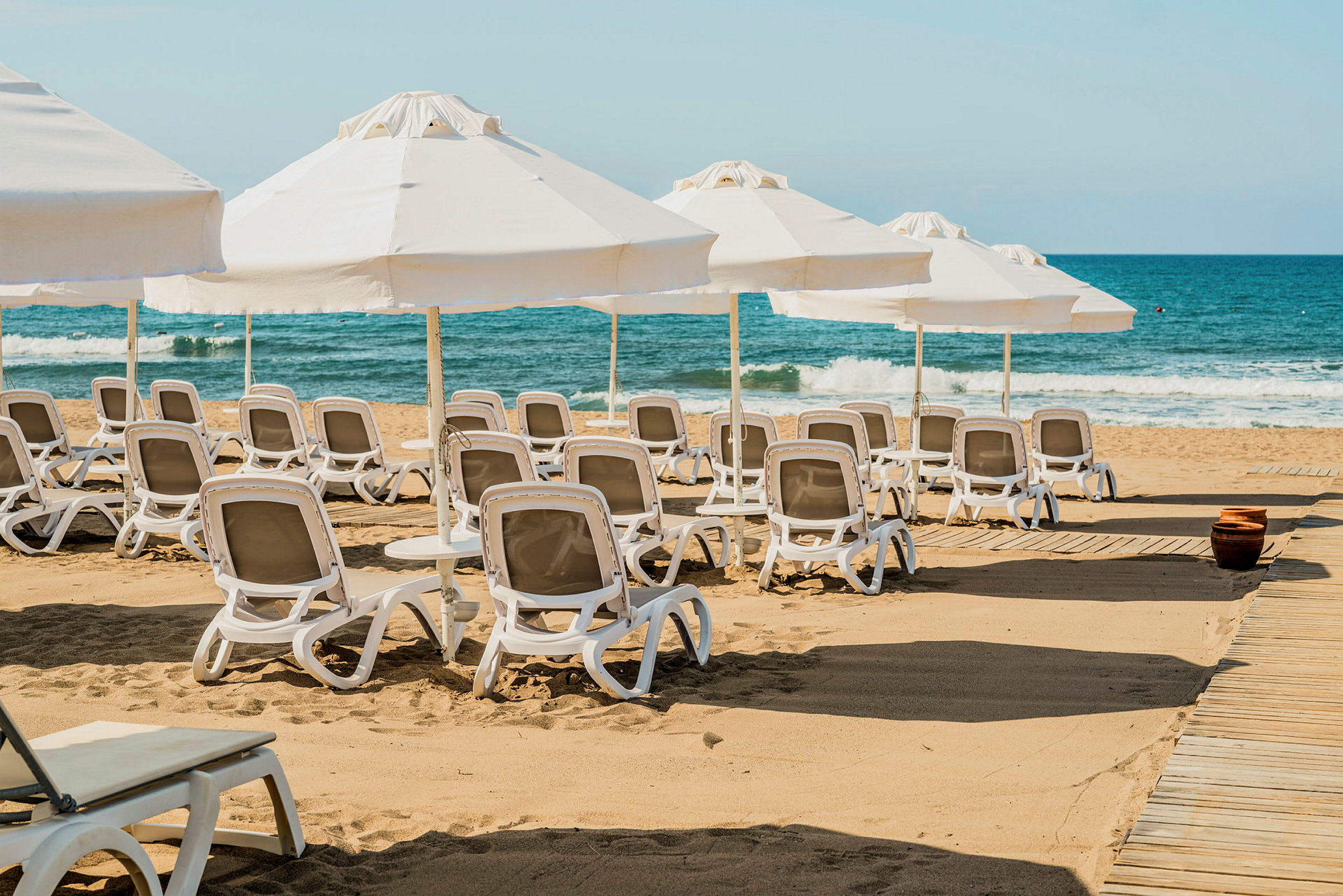 Solstolar och parasoller på en sandstrand med vågor i bakgrunden. (AI-genererad text)