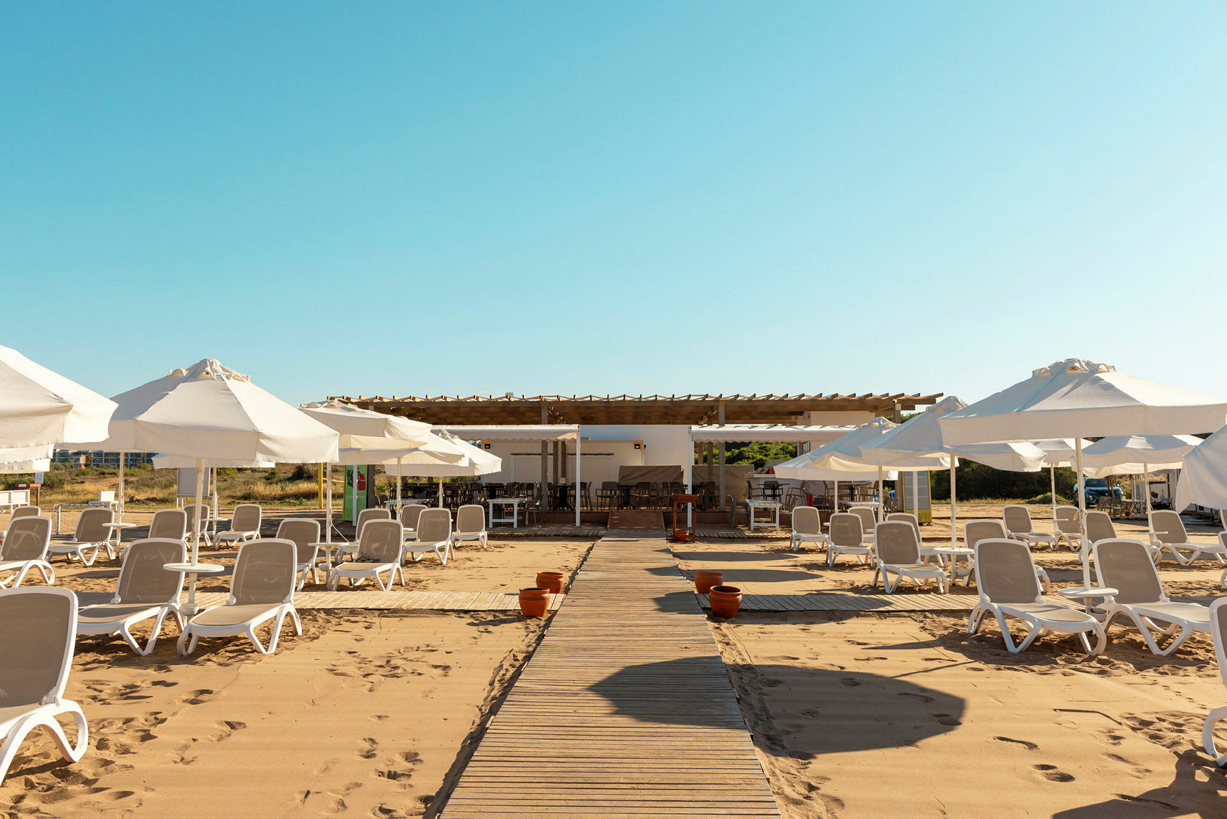 En strand med solstolar och parasoller på sanden, samt en strandbar i bakgrunden. (AI-genererad text)