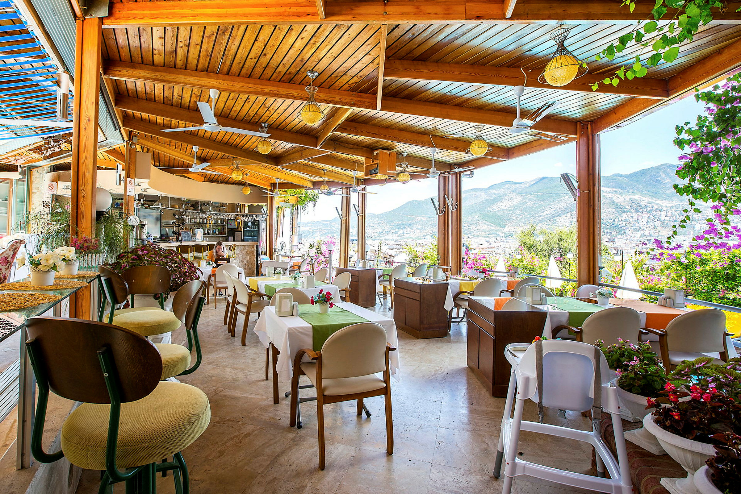 En restaurang med utsikt över bergen och staden, med bord dekorerade med blommor. (AI-genererad text)