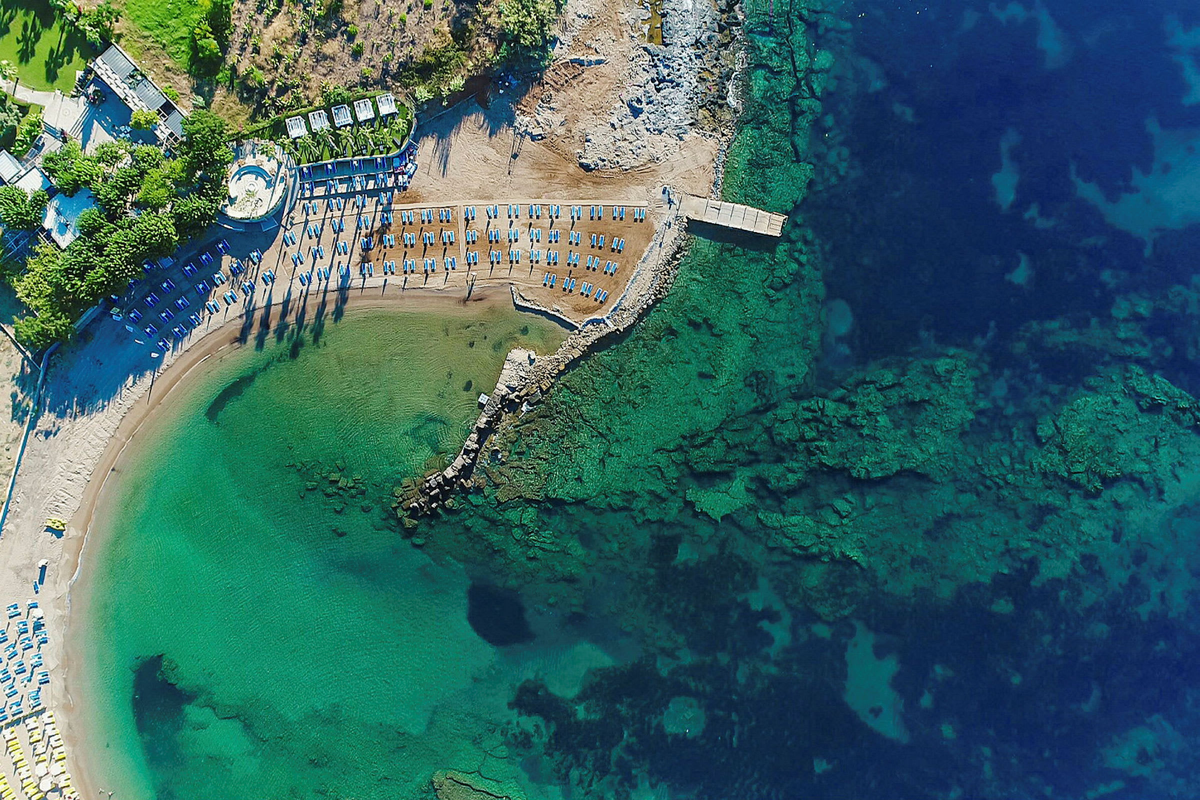 Flygbild av en strand med solstolar och parasoller vid en turkost hav. (AI-genererad text)