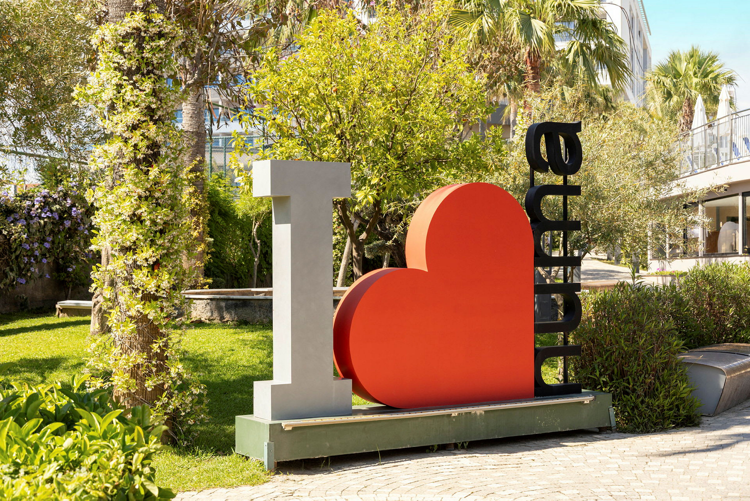 Skulpturen föreställer texten "I ♡ Alanya" omgivet av en lummig trädgård. (AI-genererad text)