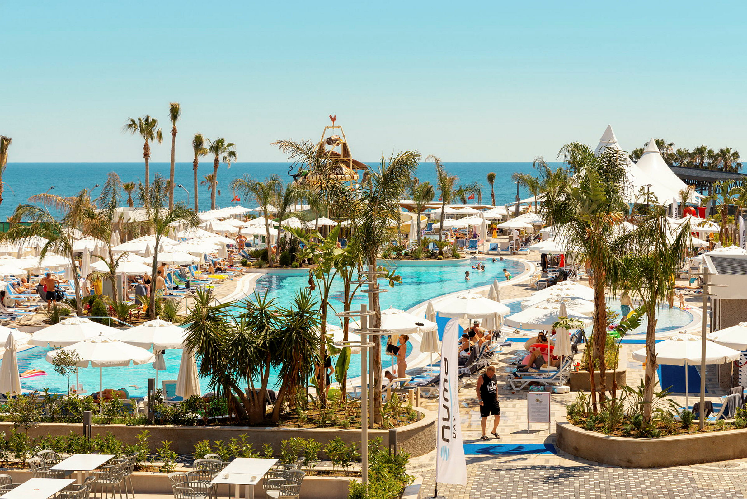Poolområde vid ett semesterhotell med solstolar, parasoller och utsikt över havet. (AI-genererad text)