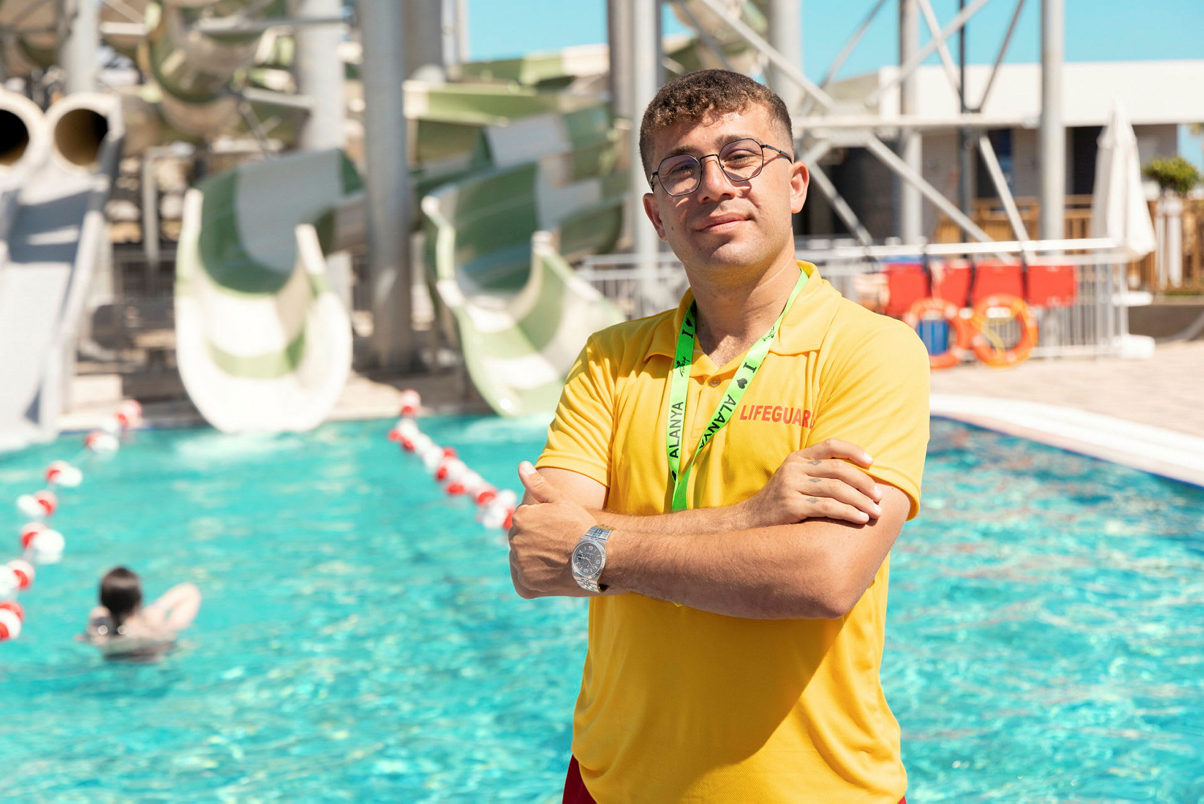 En badvakt står vid en pool framför vattenrutschbanor. (AI-genererad text)