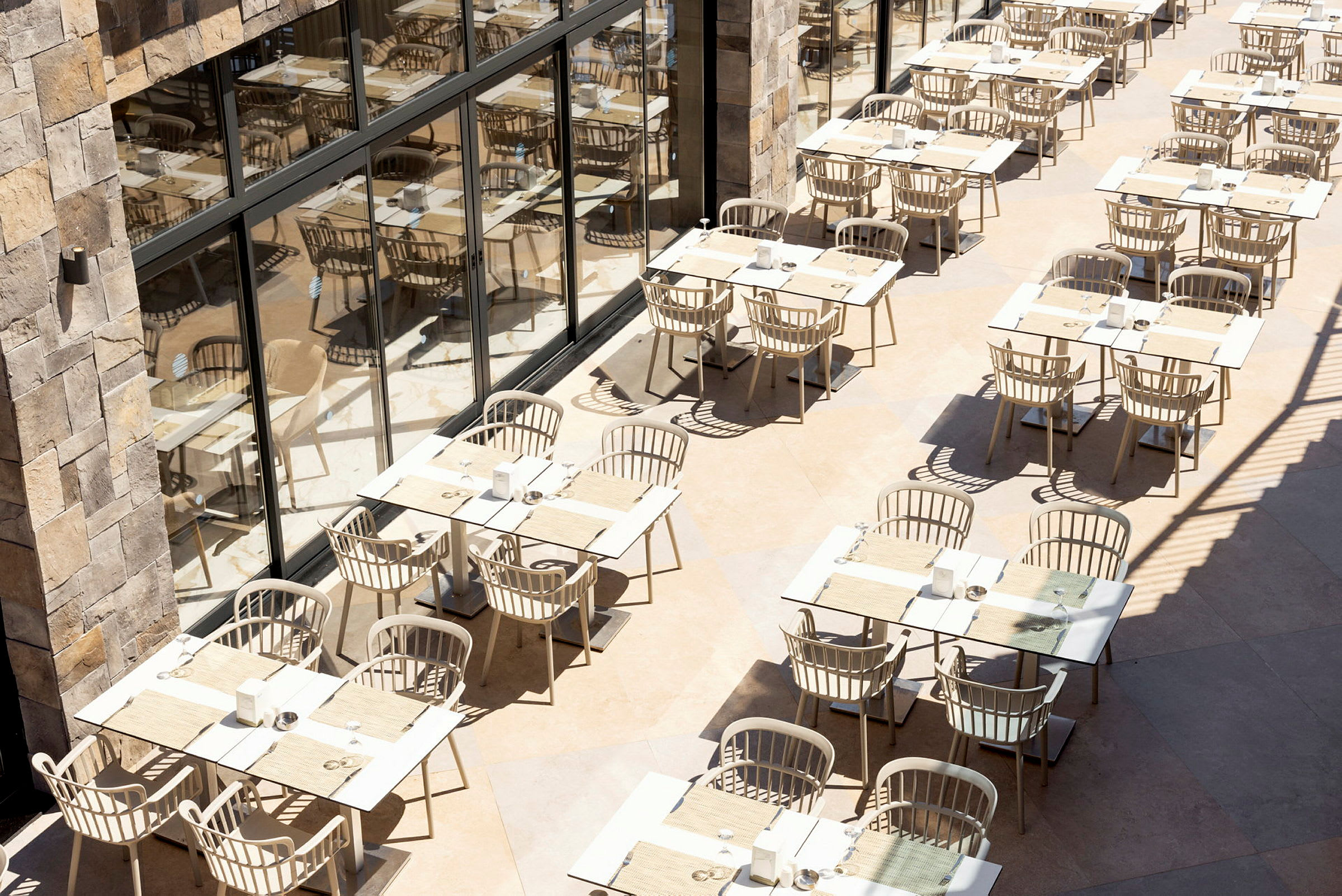 Utomhusrestaurang med bord och stolar ordnade i rader nära en byggnad med glasväggar. (AI-genererad text)