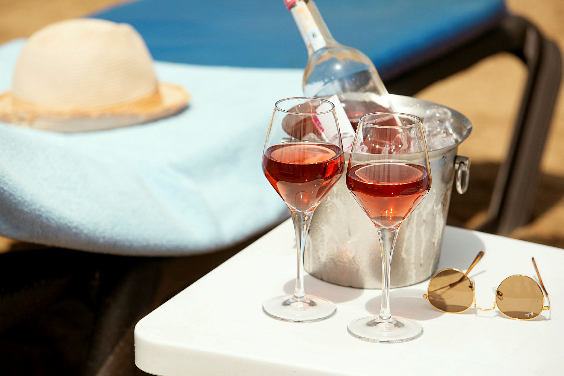Två glas rosévin och en kylhink med vinflaska på ett bord vid en solstol. (AI-genererad text)