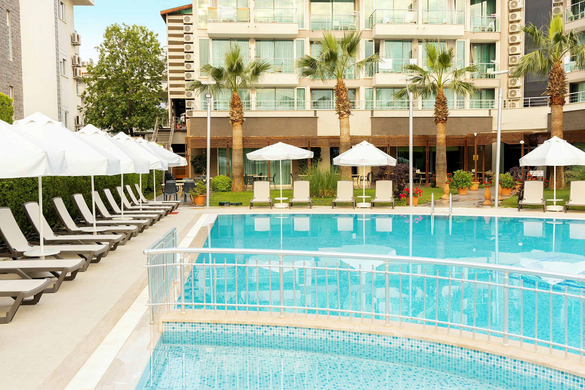 Utomhuspool med solstolar och parasoller framför ett hotell. (AI-genererad text)