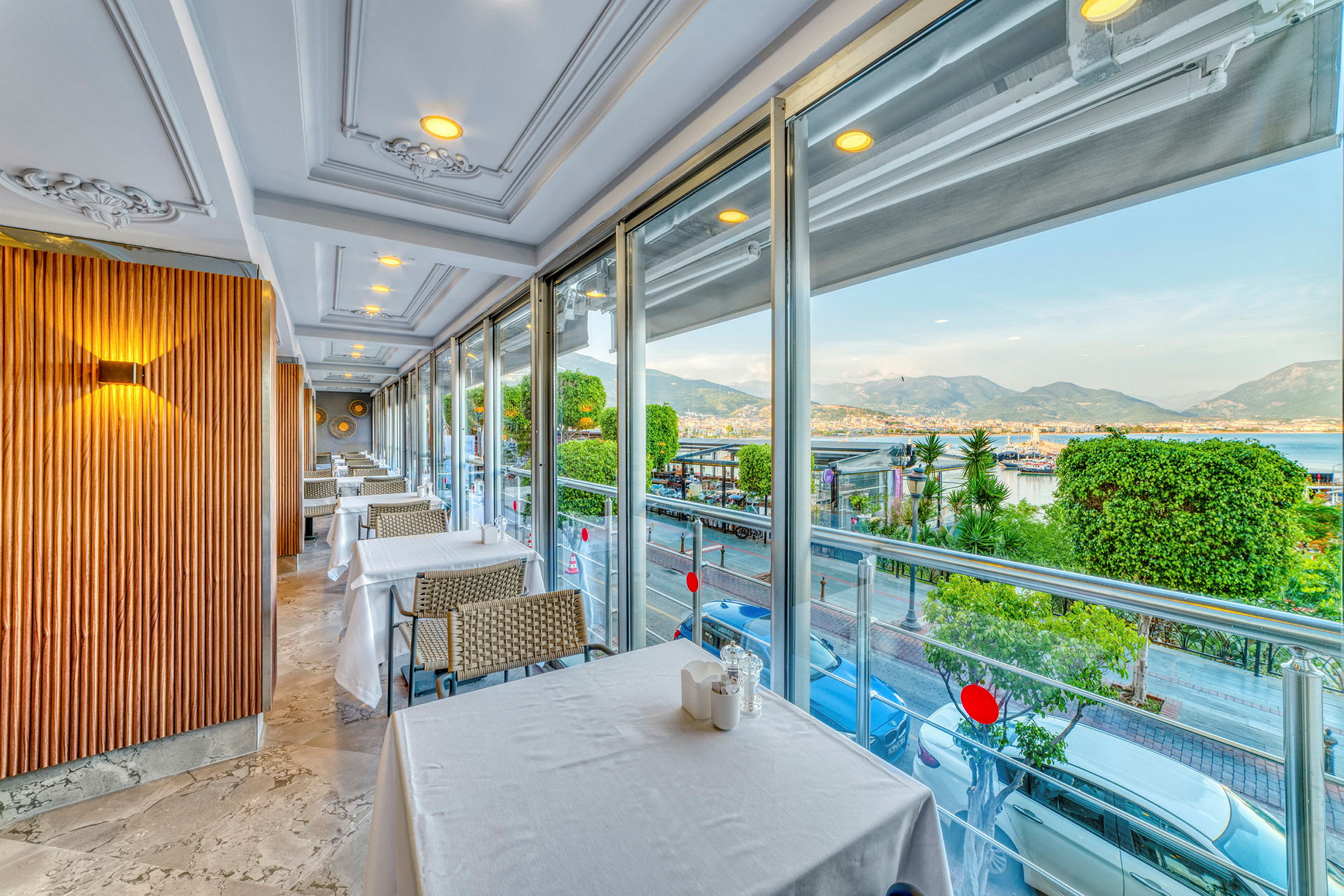 Restaurang med dukade bord och utsikt över havet och en stad. (AI-genererad text)