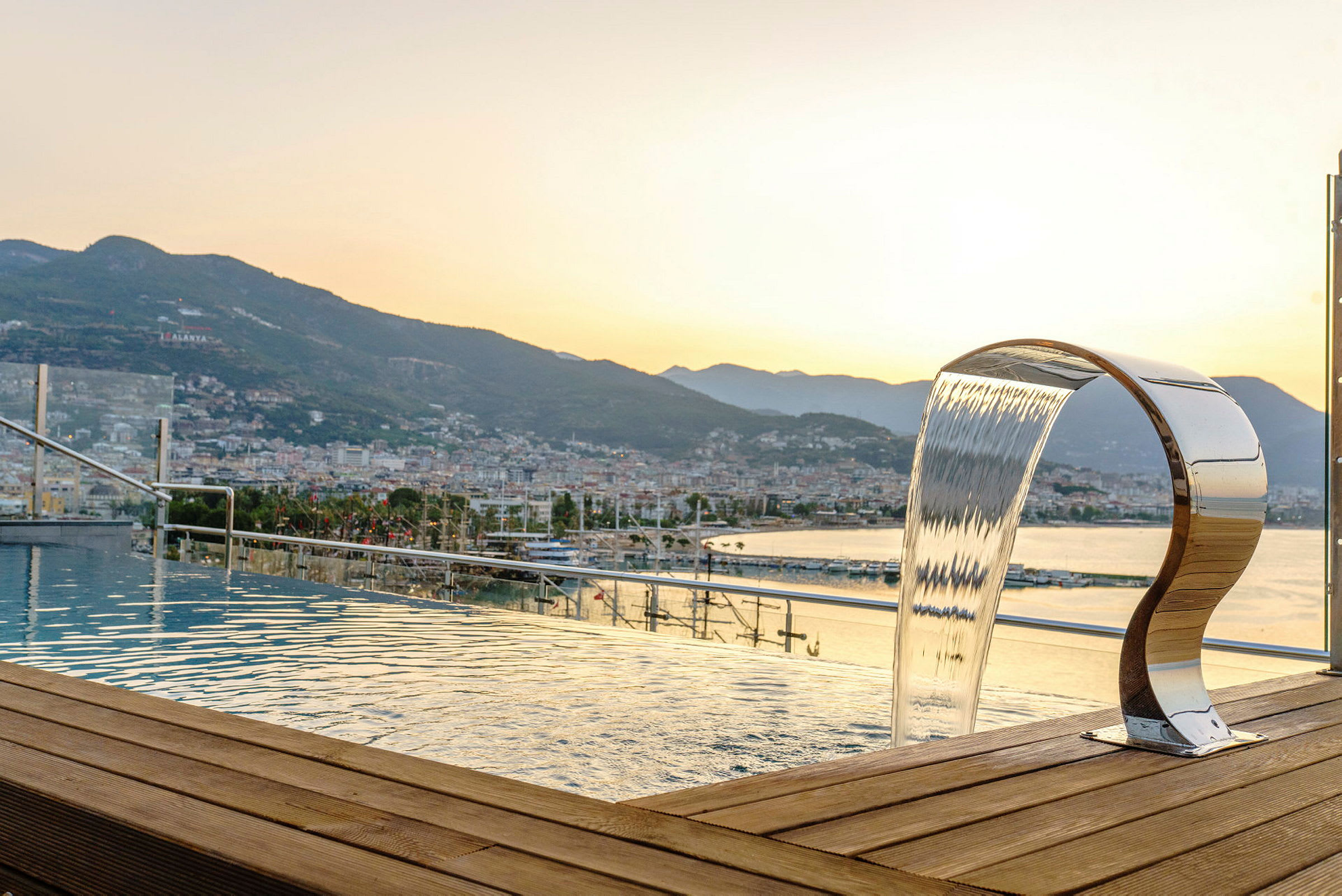 Utsikt över staden och bergen från en infinitypool med vattenfall. (AI-genererad text)