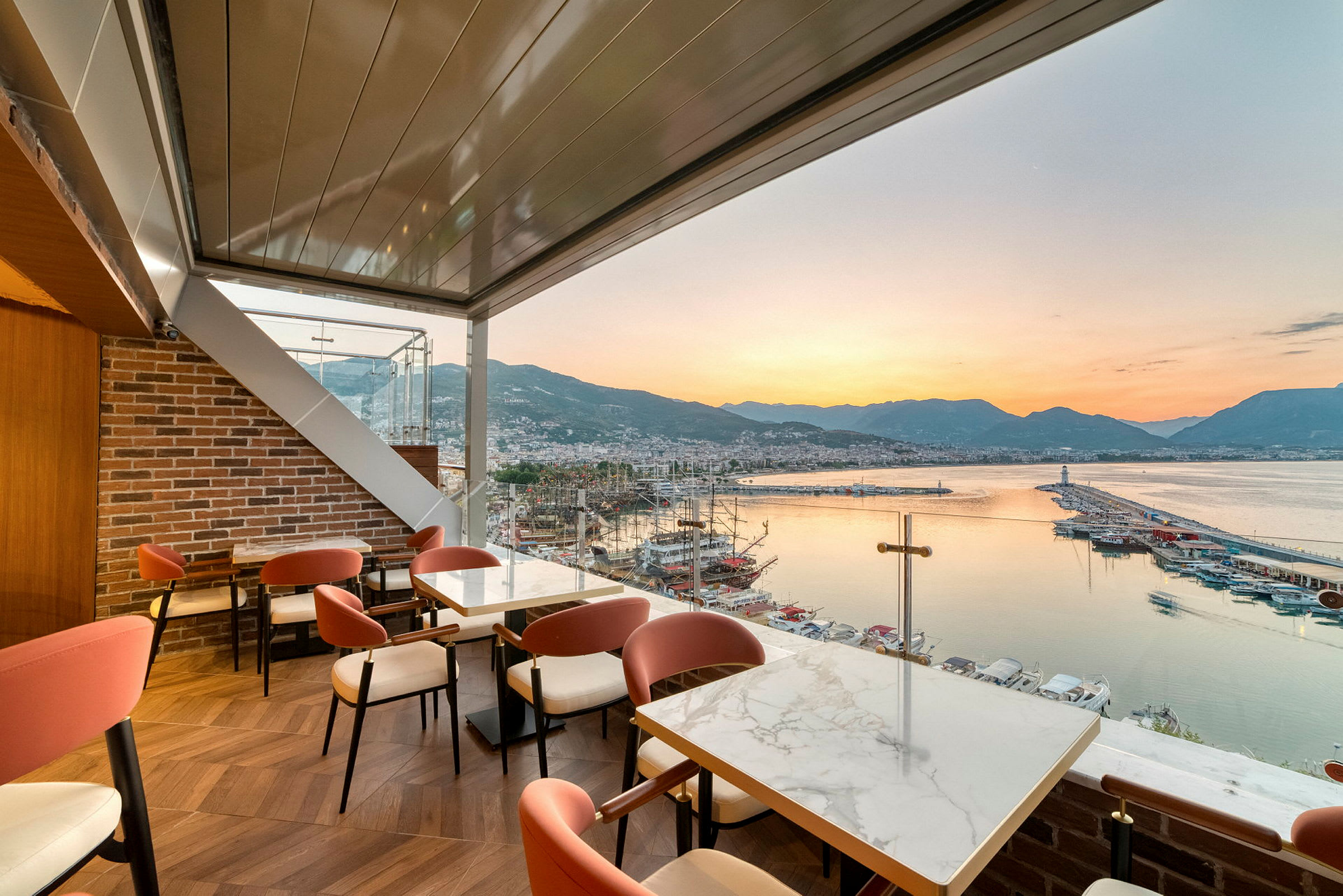 Restaurang med utsikt över en hamn, havet och bergen vid solnedgång. (AI-genererad text)