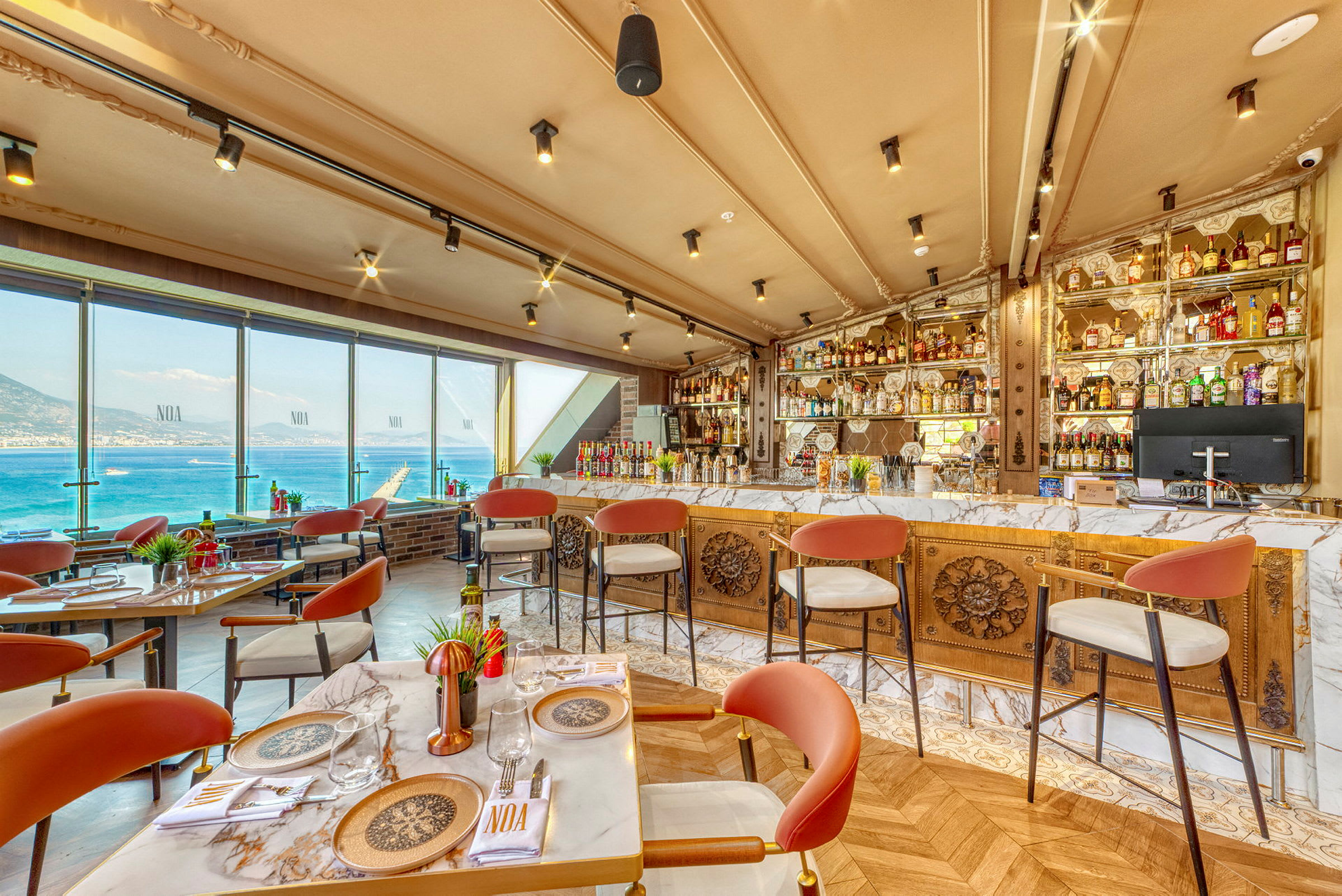 Restaurang med utsikt över havet, bord och stolar, samt en välfylld bar. (AI-genererad text)