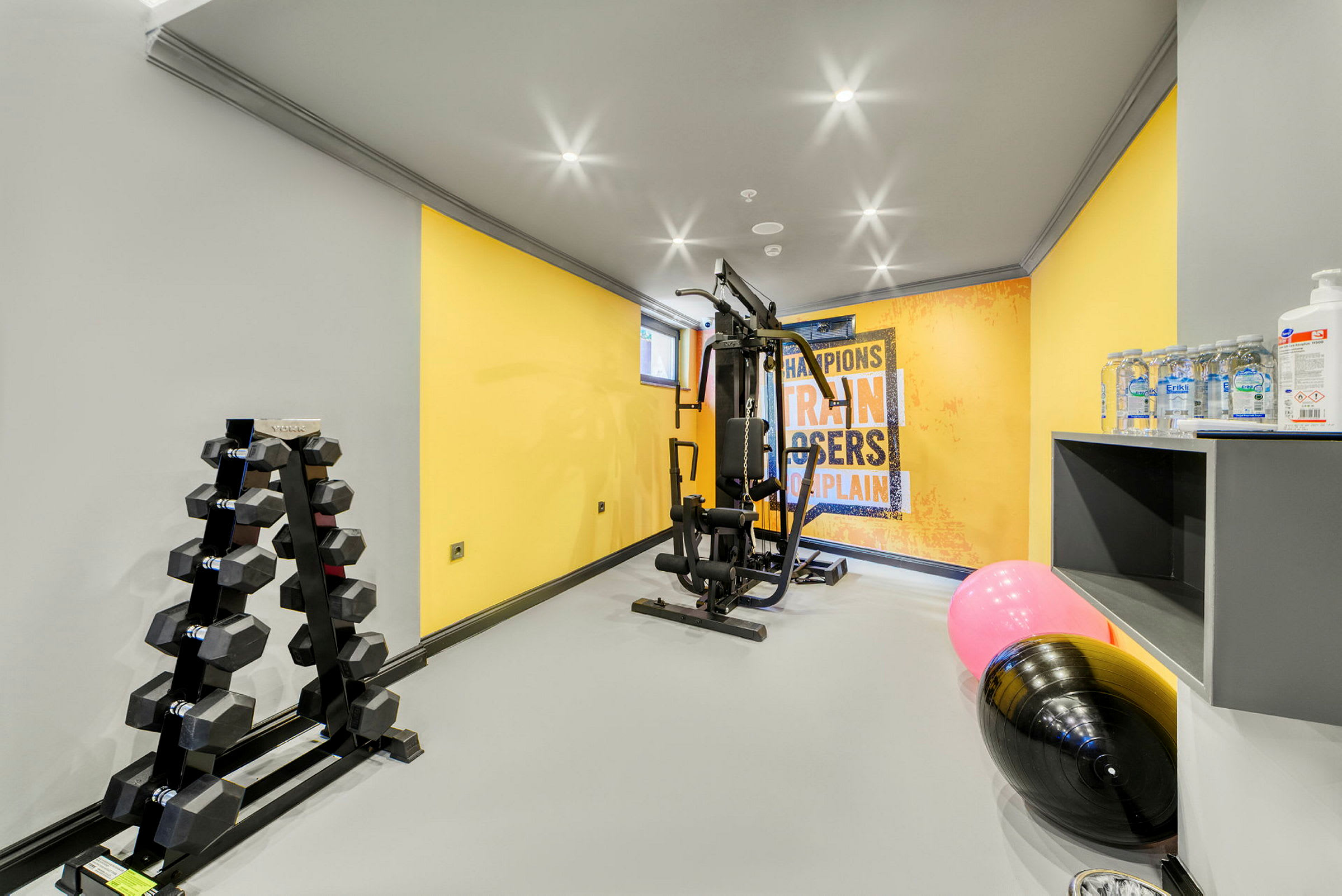 Ett gym med träningsutrustning, hantlar, en affisch på väggen och vattenflaskor. (AI-genererad text)