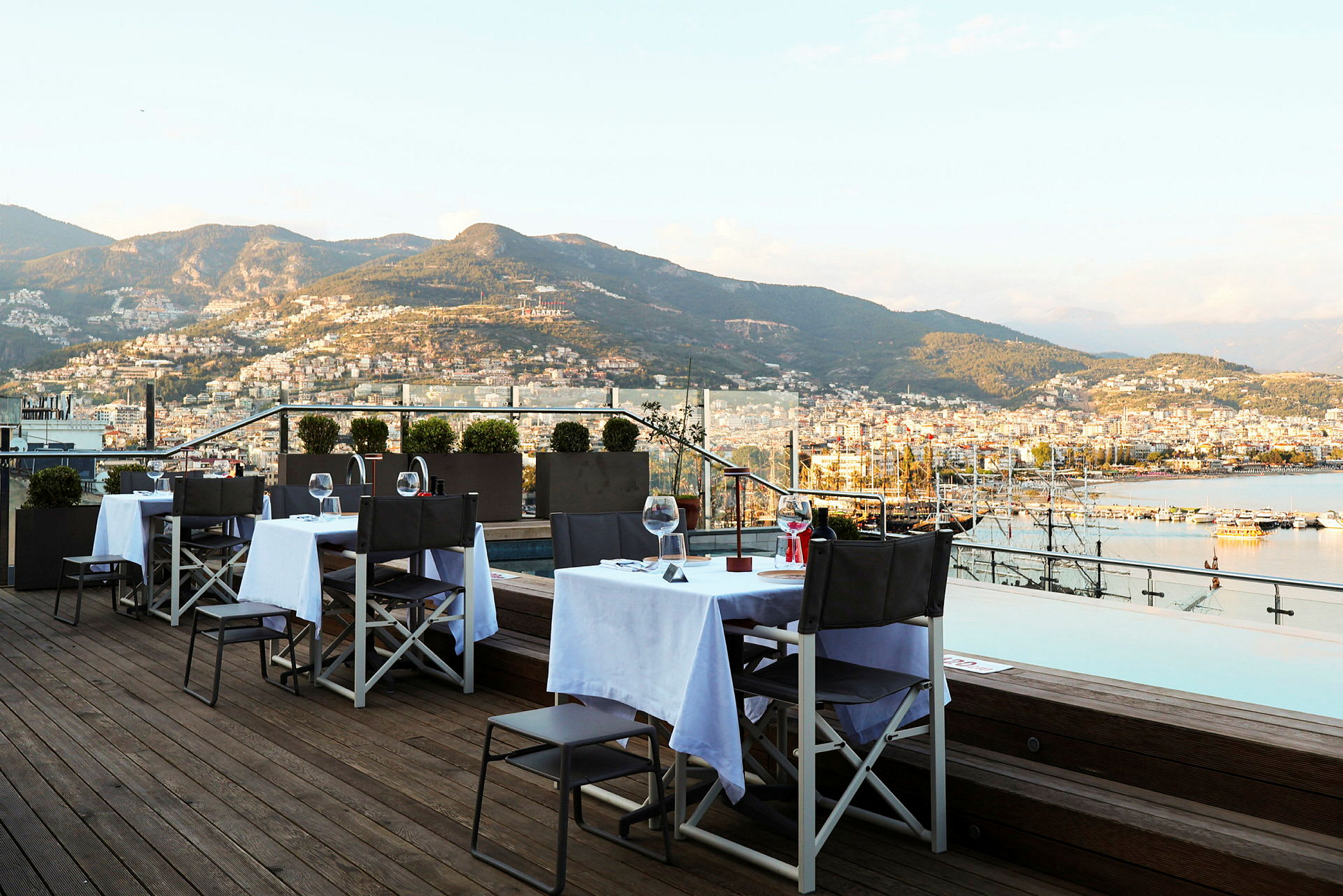 Restaurangbord på en terrass med utsikt över berg och hav. (AI-genererad text)