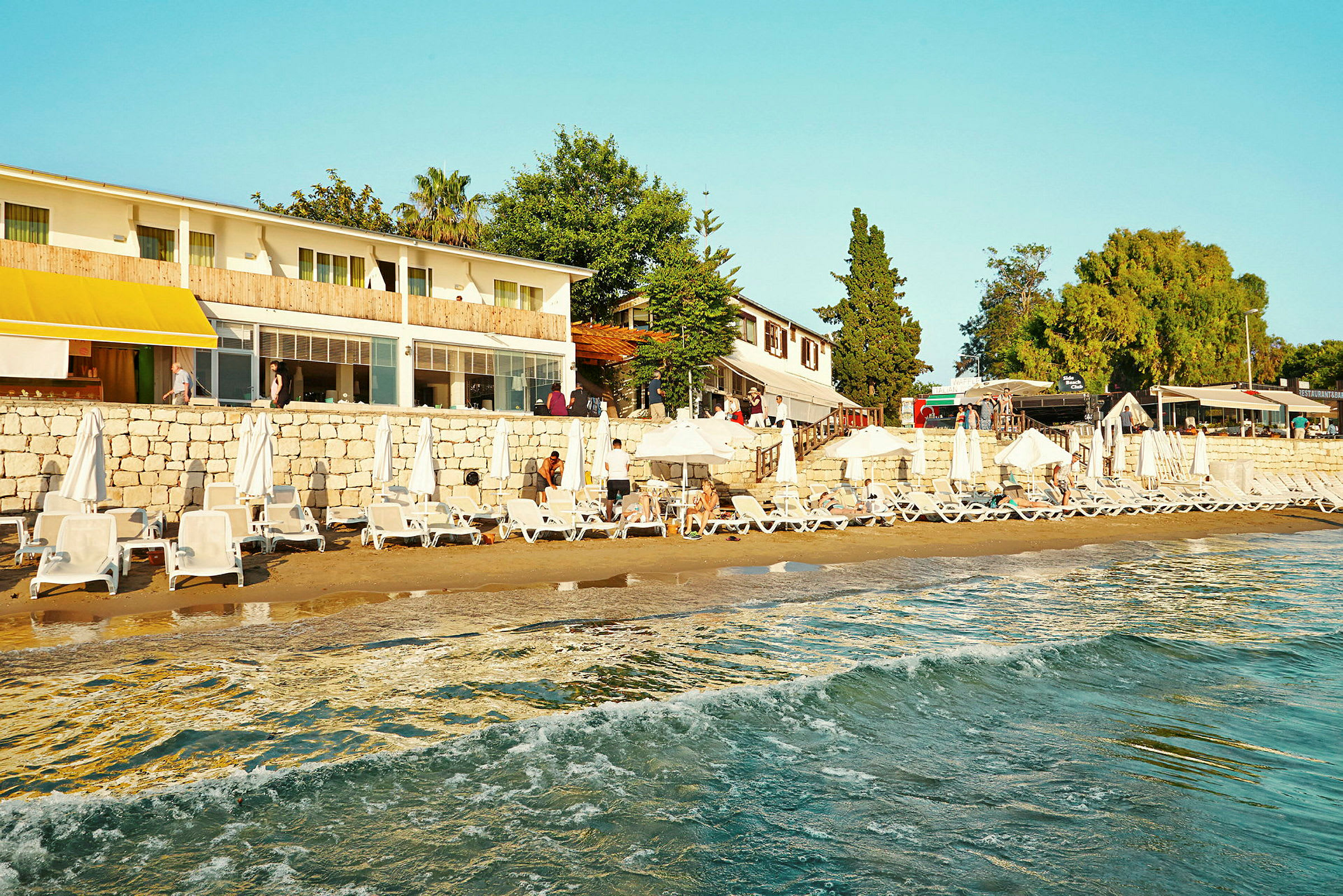Strand med solstolar och parasoller framför en byggnad och grönska. (AI-genererad text)