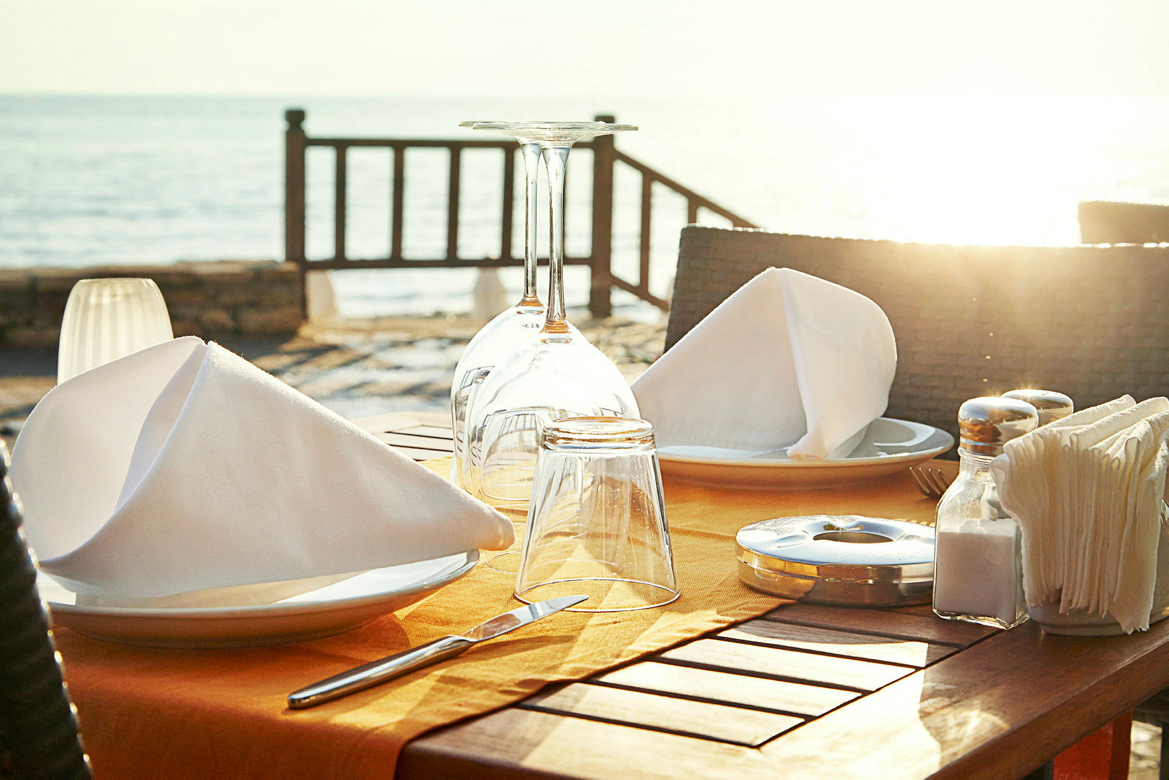 Ett dukat bord med servetter, glas och tallrikar vid havet. (AI-genererad text)