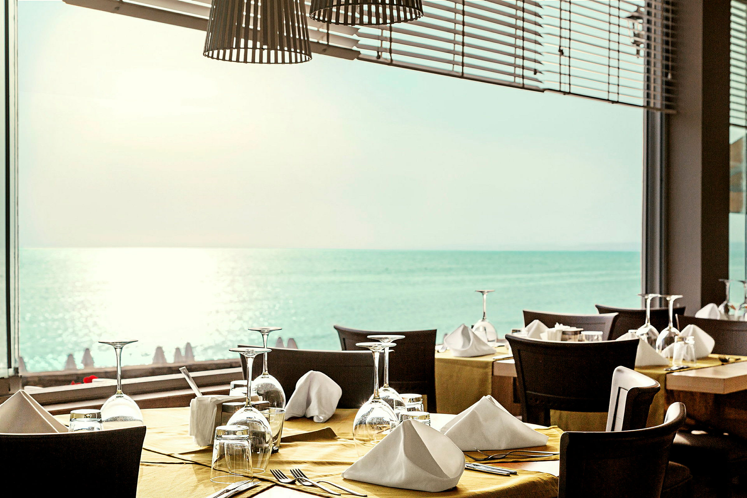 Restaurang med dukade bord framför ett fönster med utsikt över havet. (AI-genererad text)