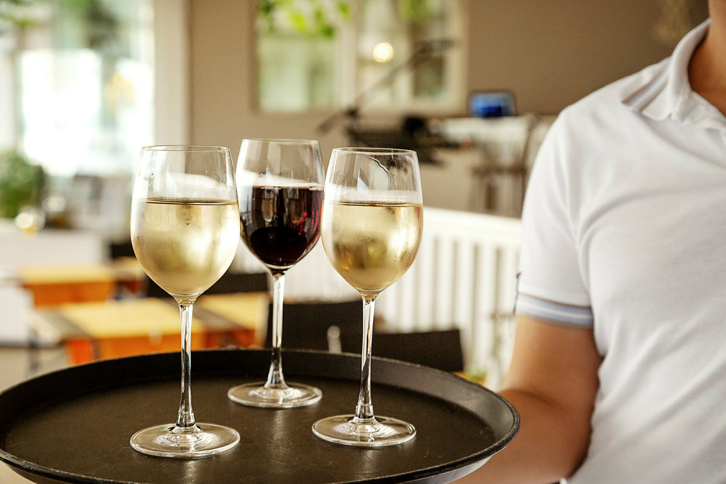En person håller en bricka med tre vinglas, två med vitt vin och ett med rött vin. (AI-genererad text)