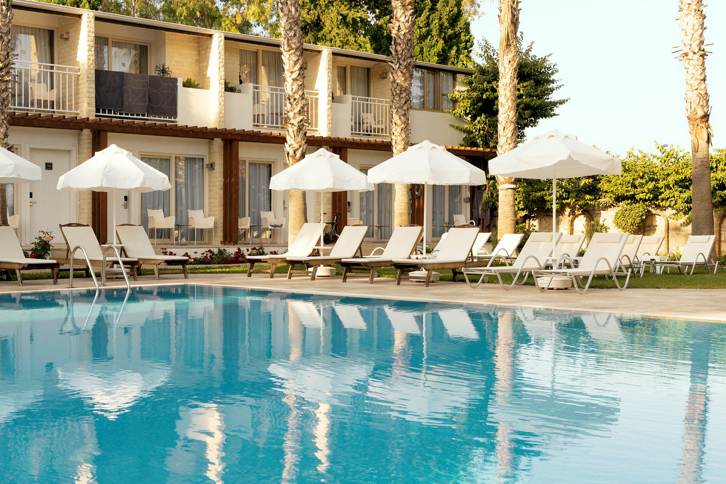 Bild av en hotellpool med solstolar och parasoller vid kanten, och byggnader i bakgrunden. (AI-genererad text)