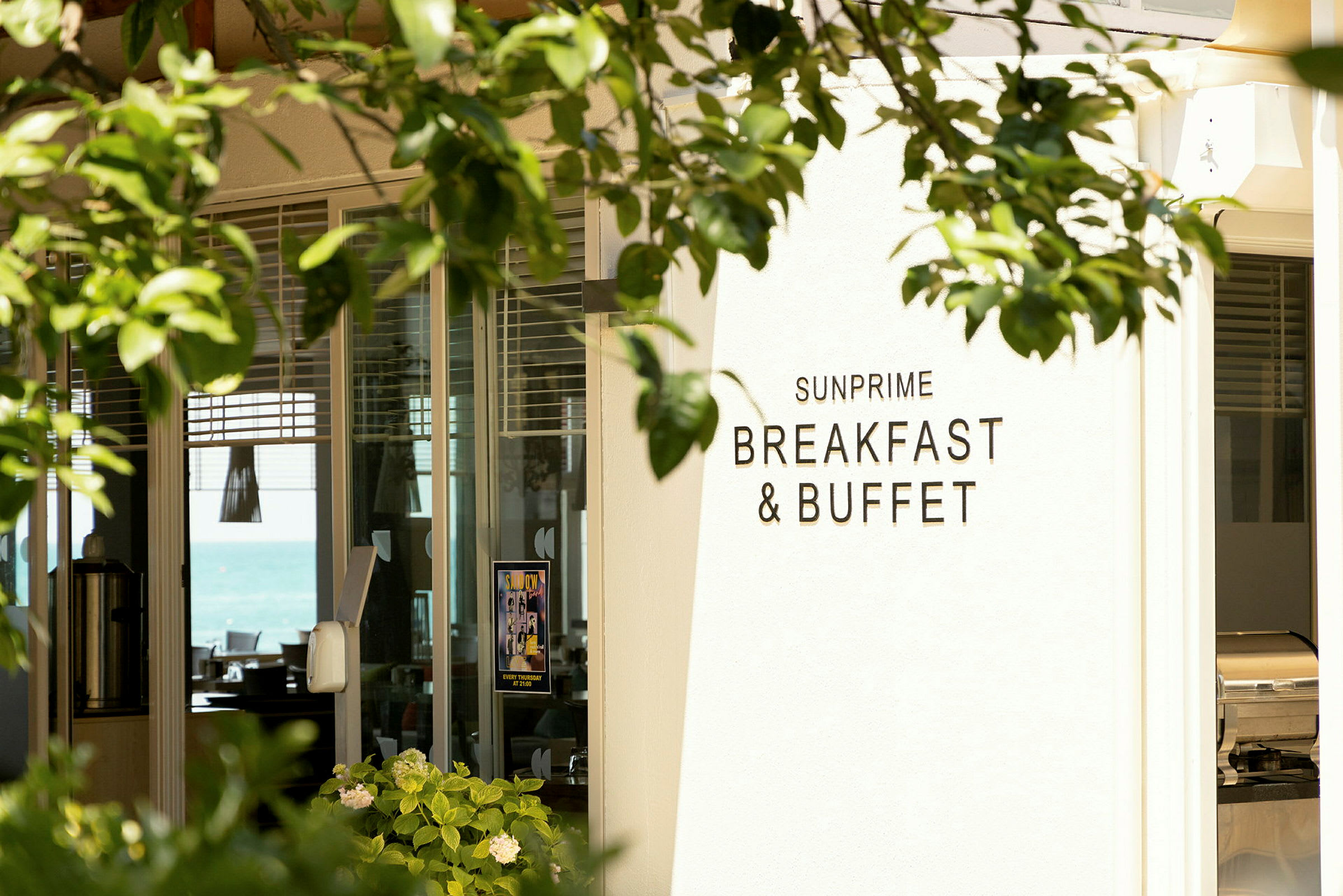 Skylt med texten 'Sunprime Breakfast & Buffet' vid ingången till en restaurant, omgiven av grönska. (AI-genererad text)