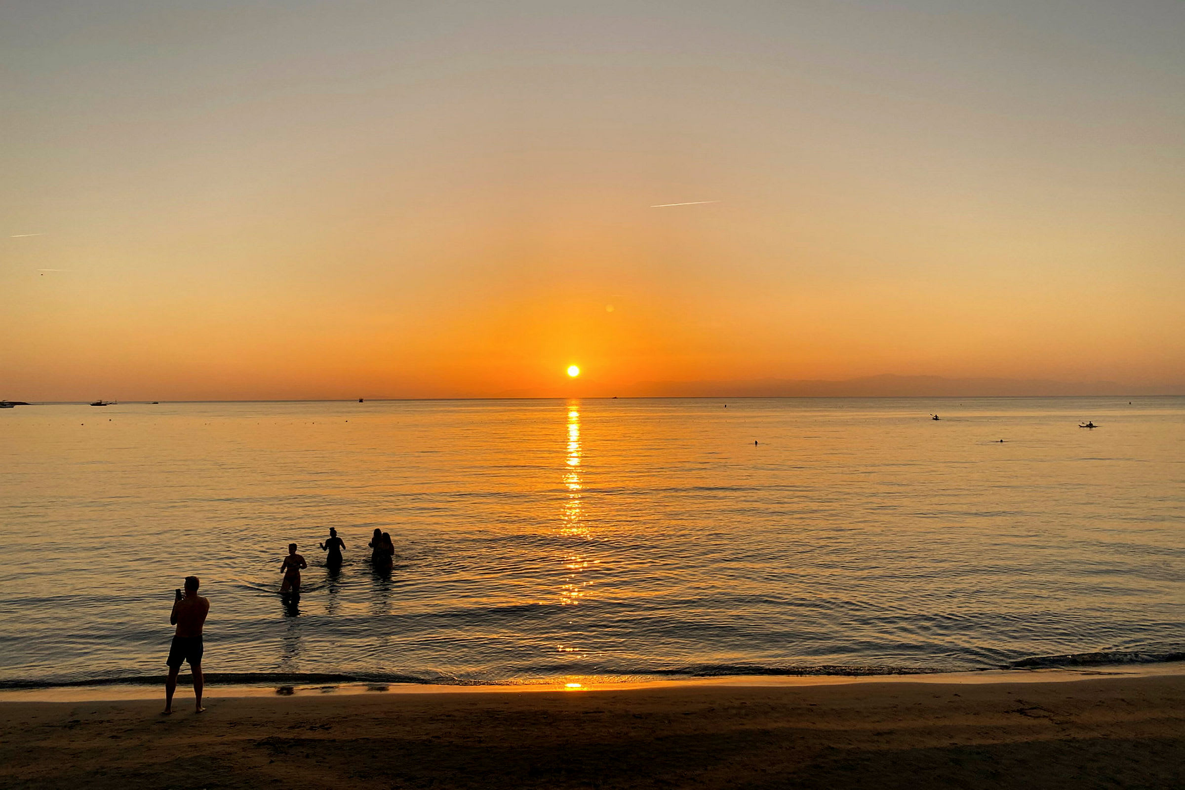 En strand vid solnedgången med människor i vattnet. (AI-genererad text)